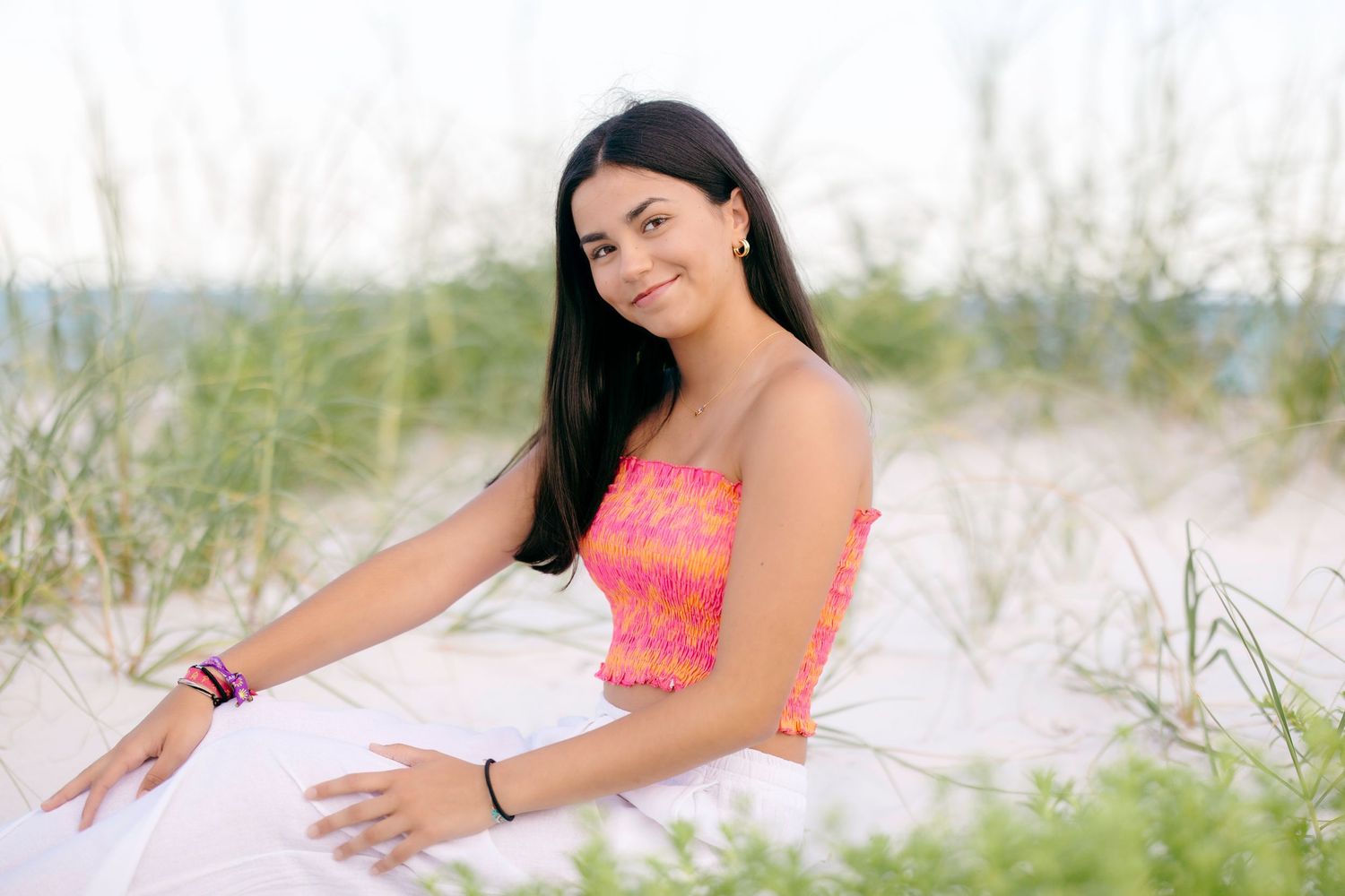 Casual beach portrait featuring coral pink top and white attire among sand dunes.