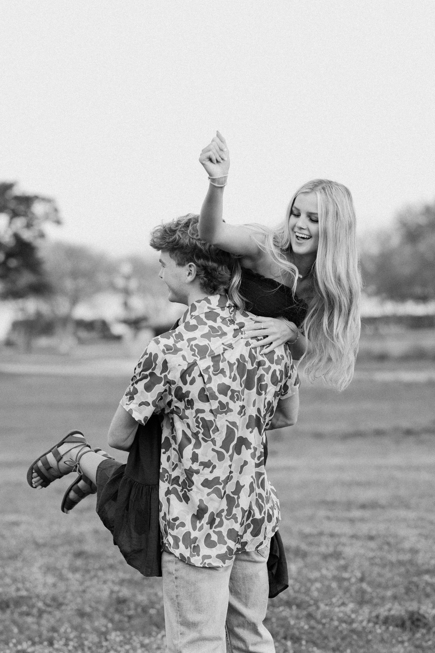 Playful couple in floral and denim outfits pose energetically against a bright outdoor background.