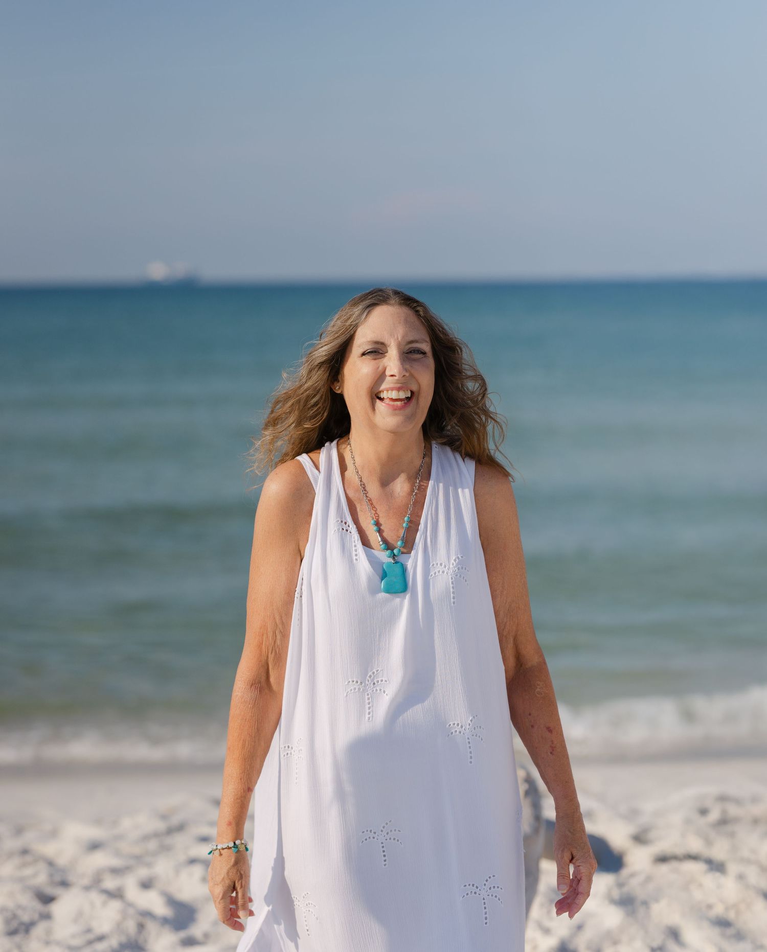 People in white clothing dance and celebrate joyfully along a beautiful beach with turquoise ocean waters.