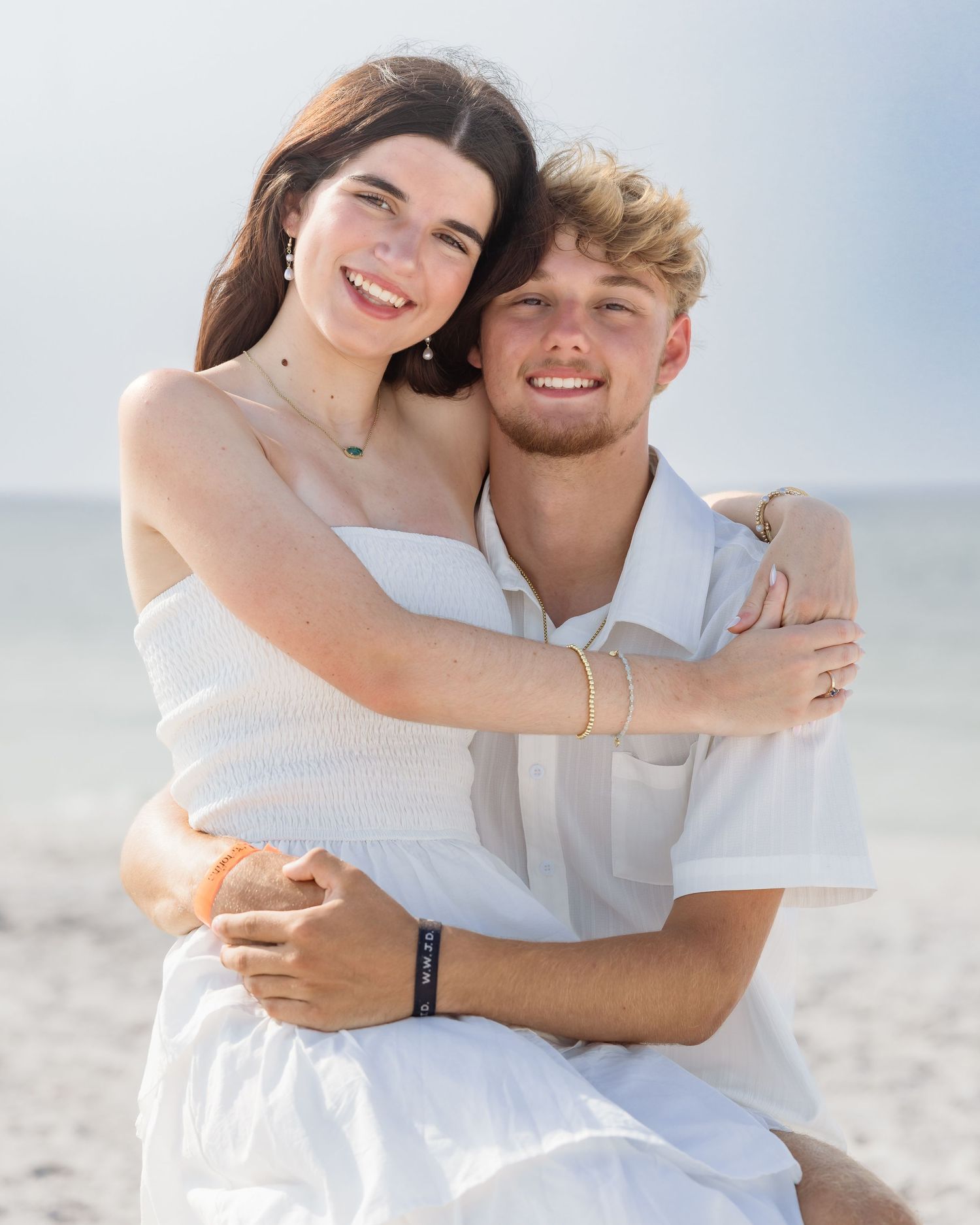 Smiling young couple hugging closely on a bright sunny beach with ocean in background.
