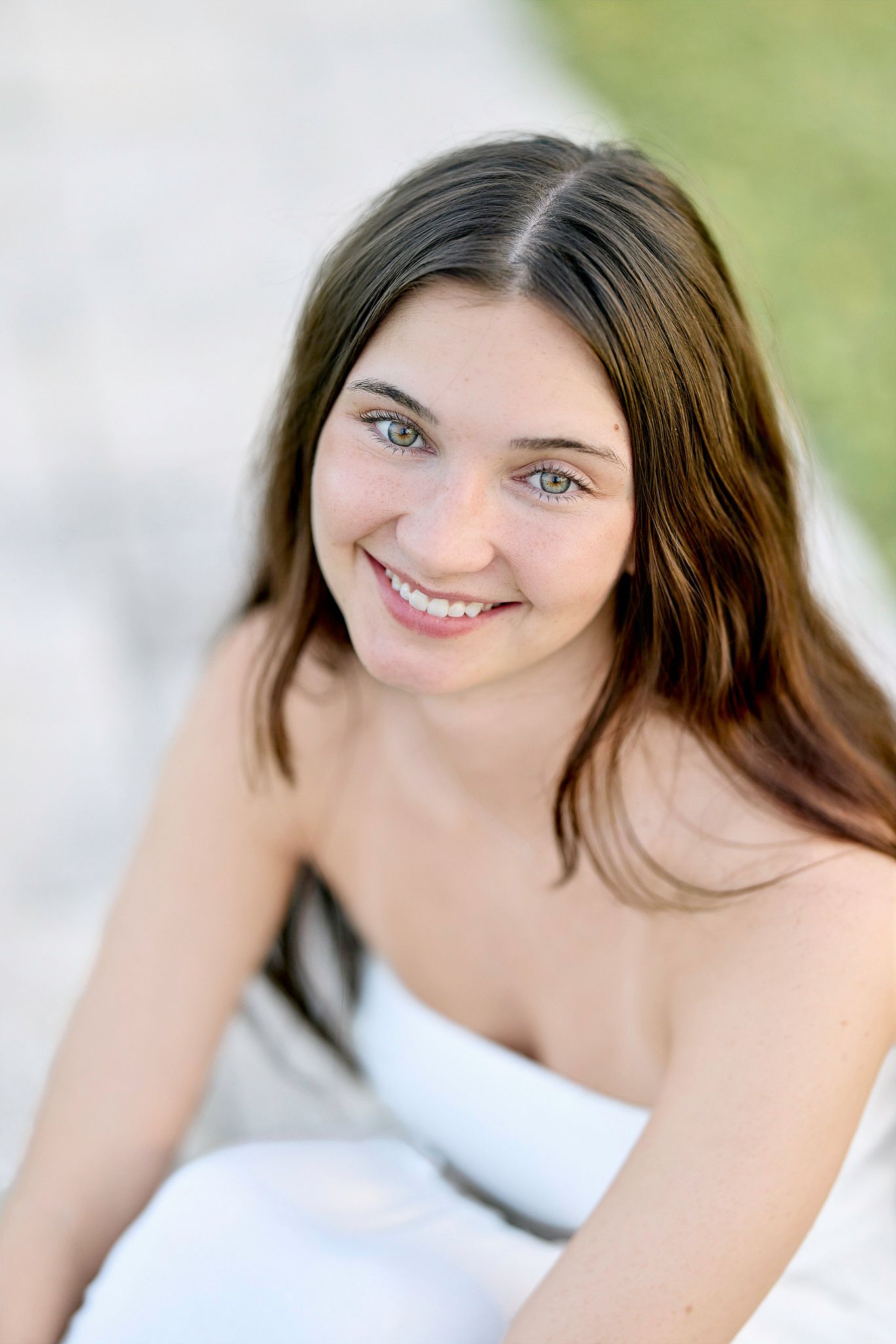 Close up portrait of a smiling woman with long brown hair wearing a white top against a light background.
