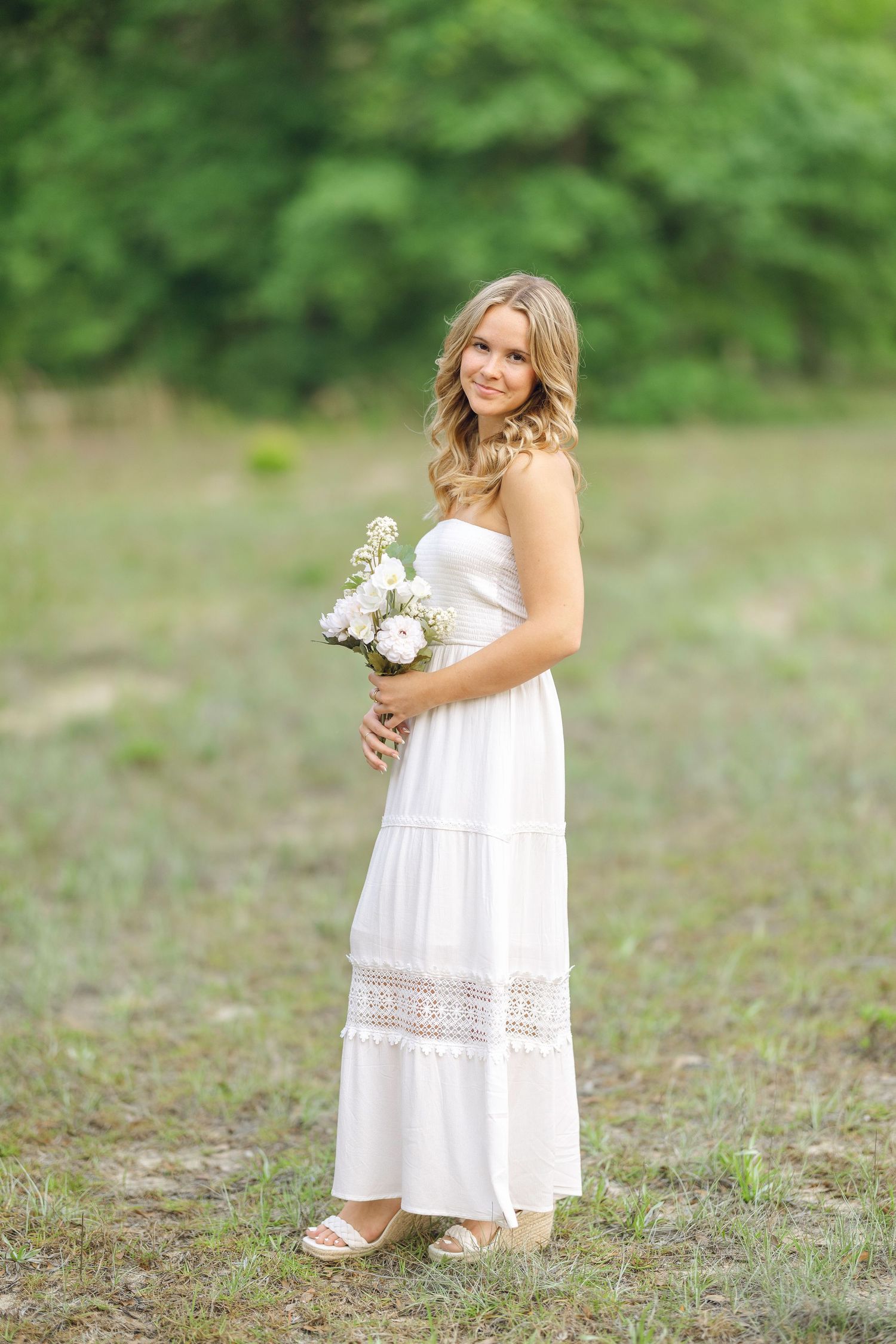 A figure in a flowing white sundress holds a bouquet of white flowers in a sunny outdoor setting.