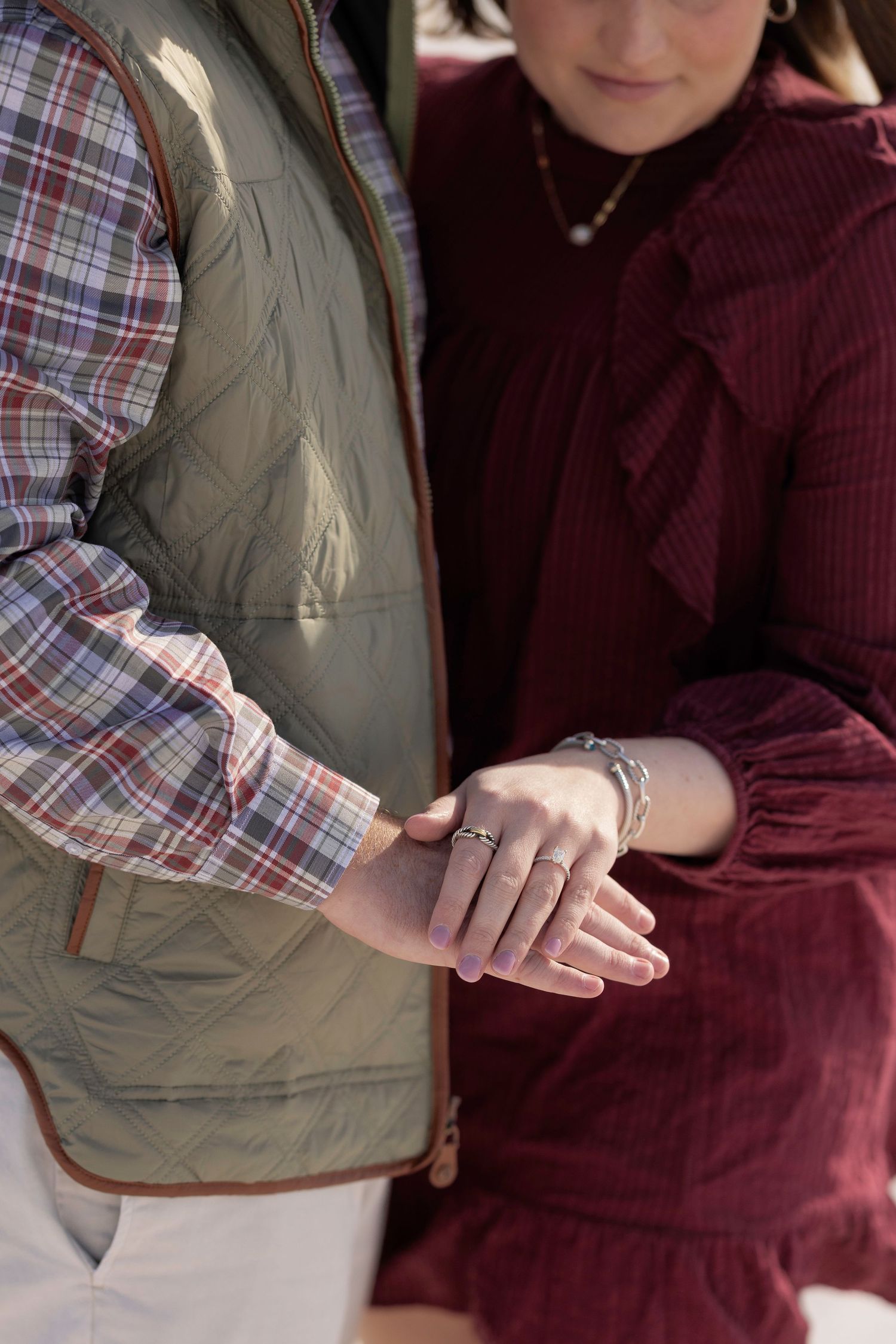 Close-up of hands holding each other while wearing plaid and burgundy colored clothing.