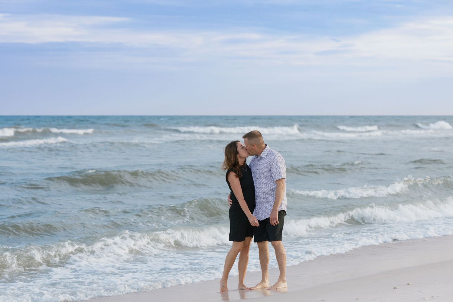 Couple sharing a romantic moment on a sandy beach with turquoise ocean waves in the background.