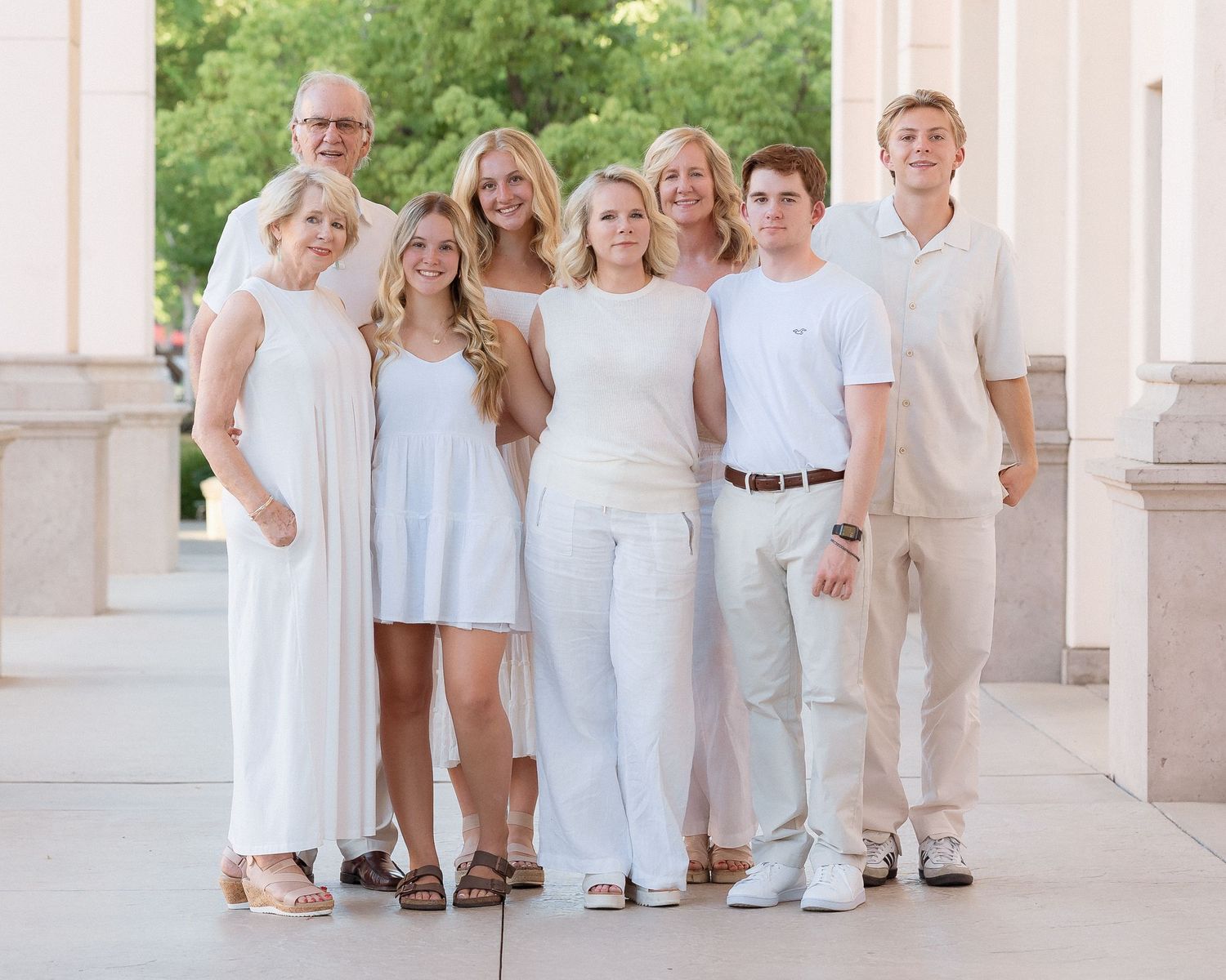 Seven family members in white and neutral tones pose together between outdoor columns.
