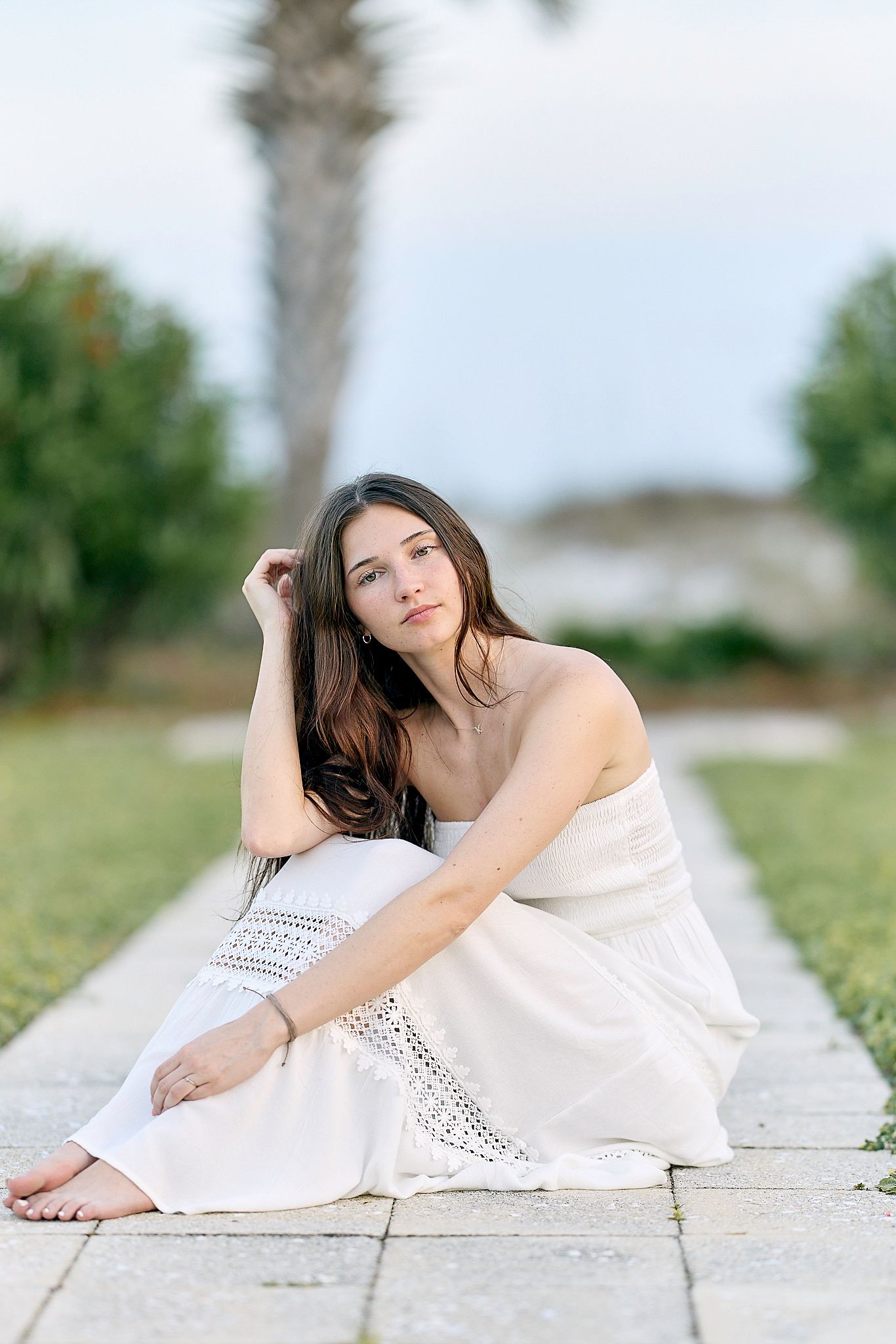 Outdoor fashion portrait with white sundress against tropical palm and garden background.