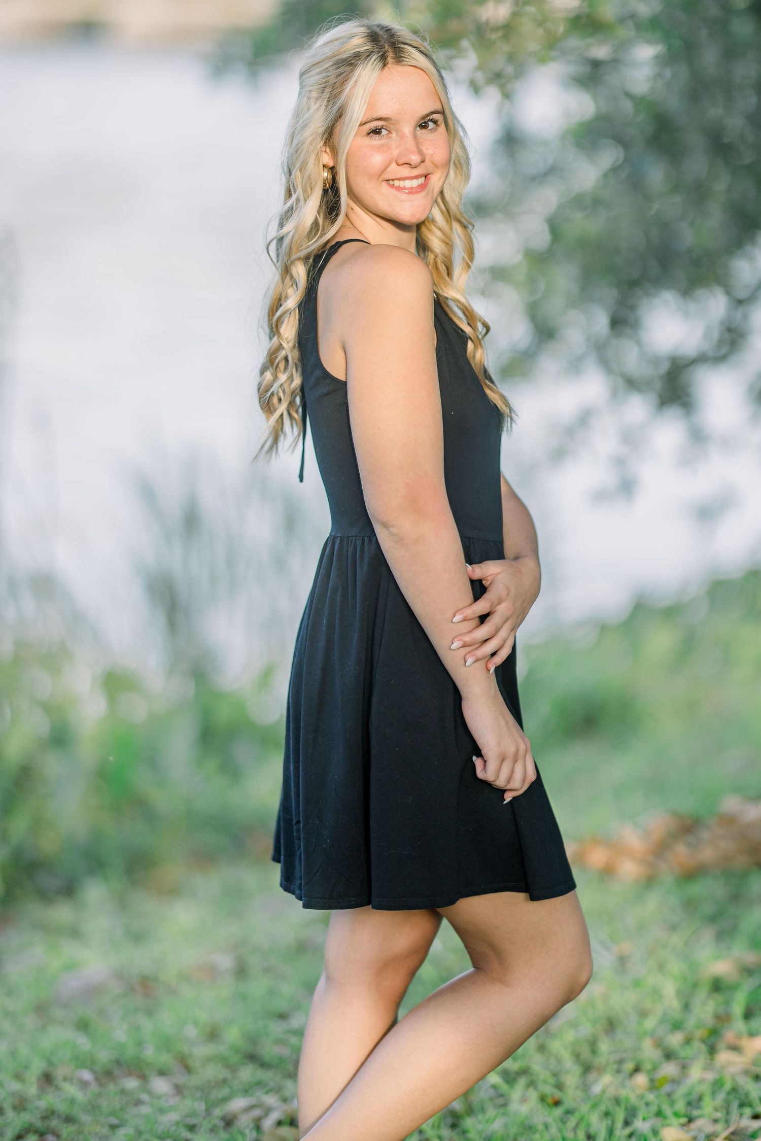Summer portrait session on grassy slopes with water and trees in the background.
