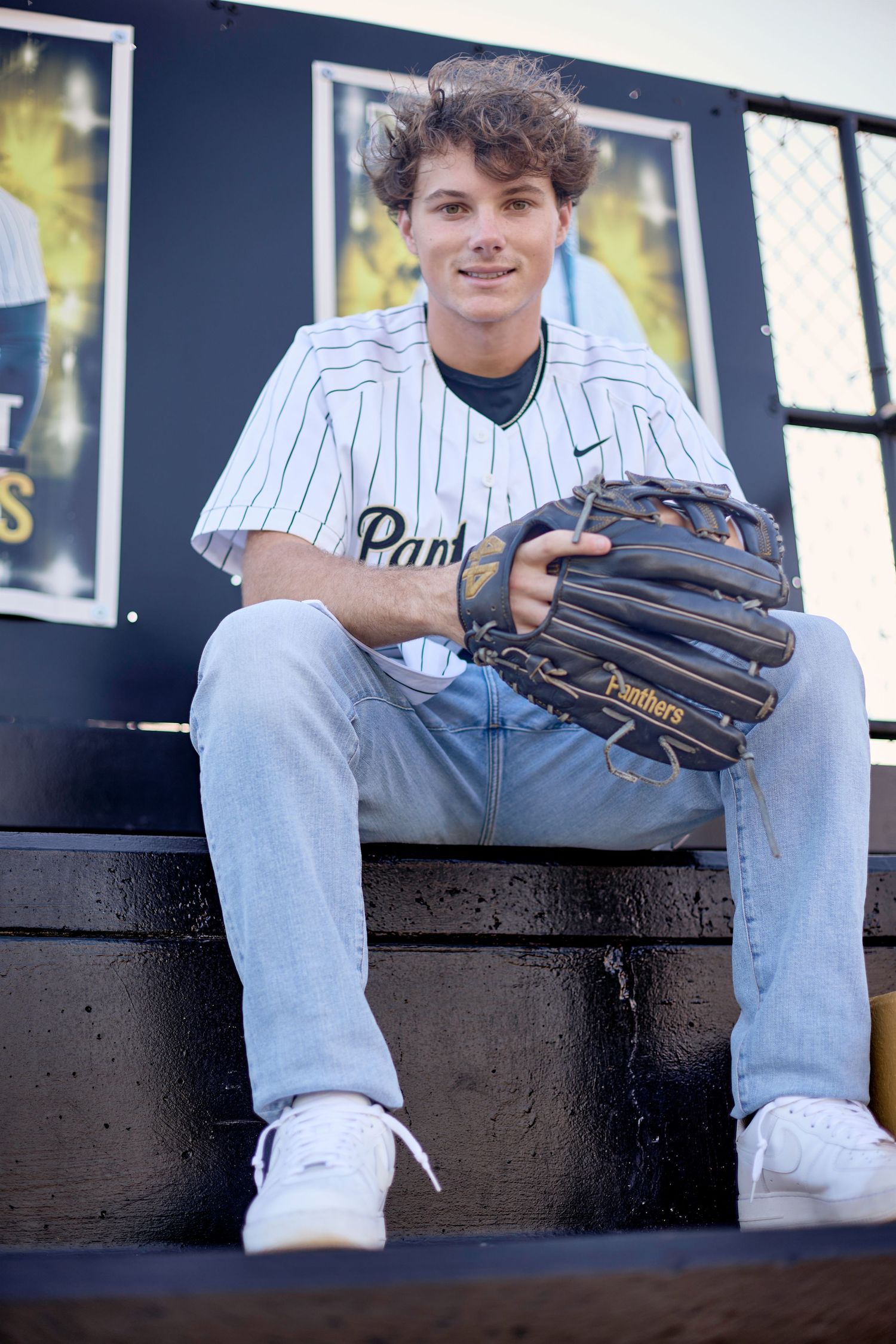 Baseball player in pinstriped uniform sitting on black surface with glove.