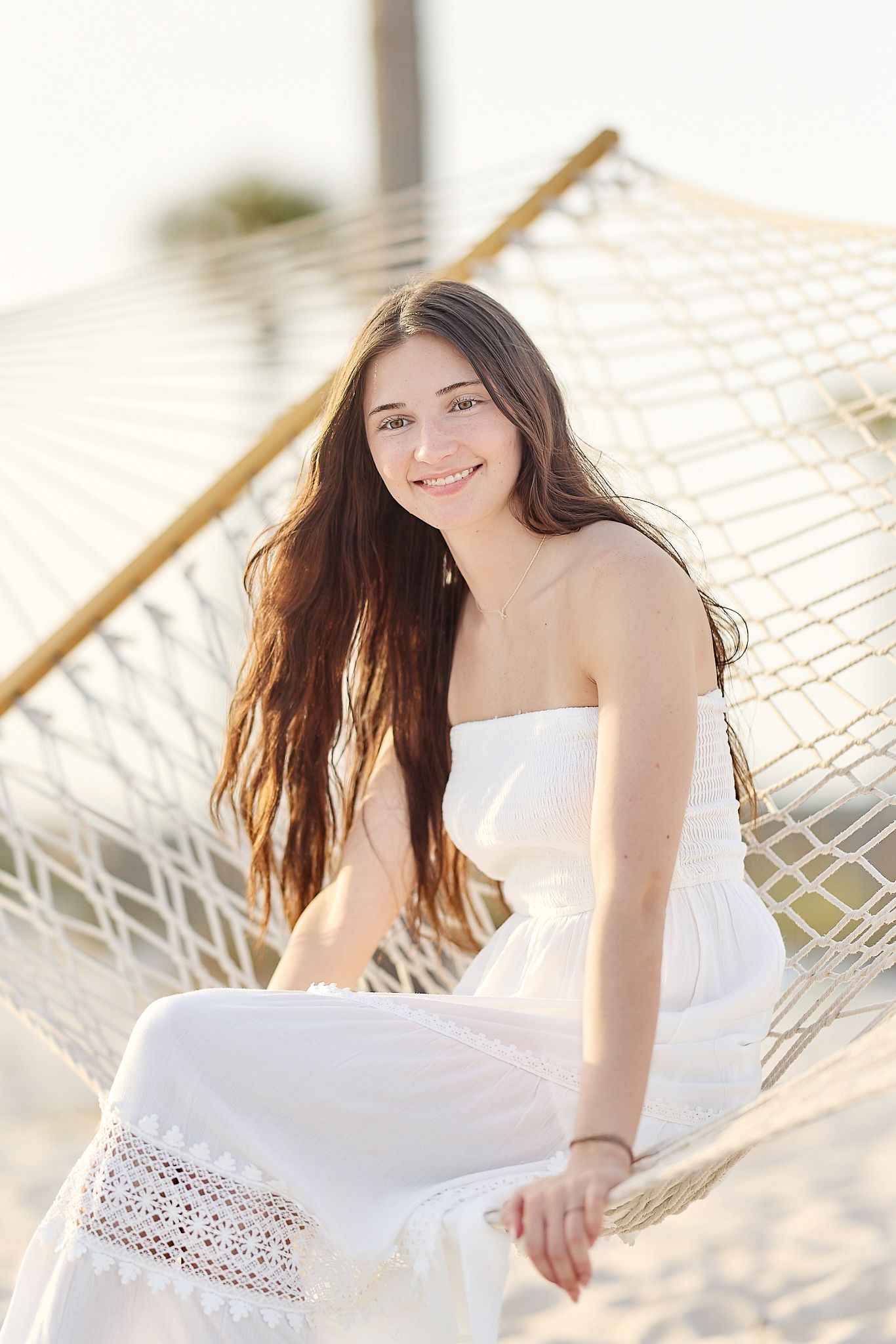 A relaxed beach photoshoot featuring a white lace-detailed maxi dress and hammock setting.