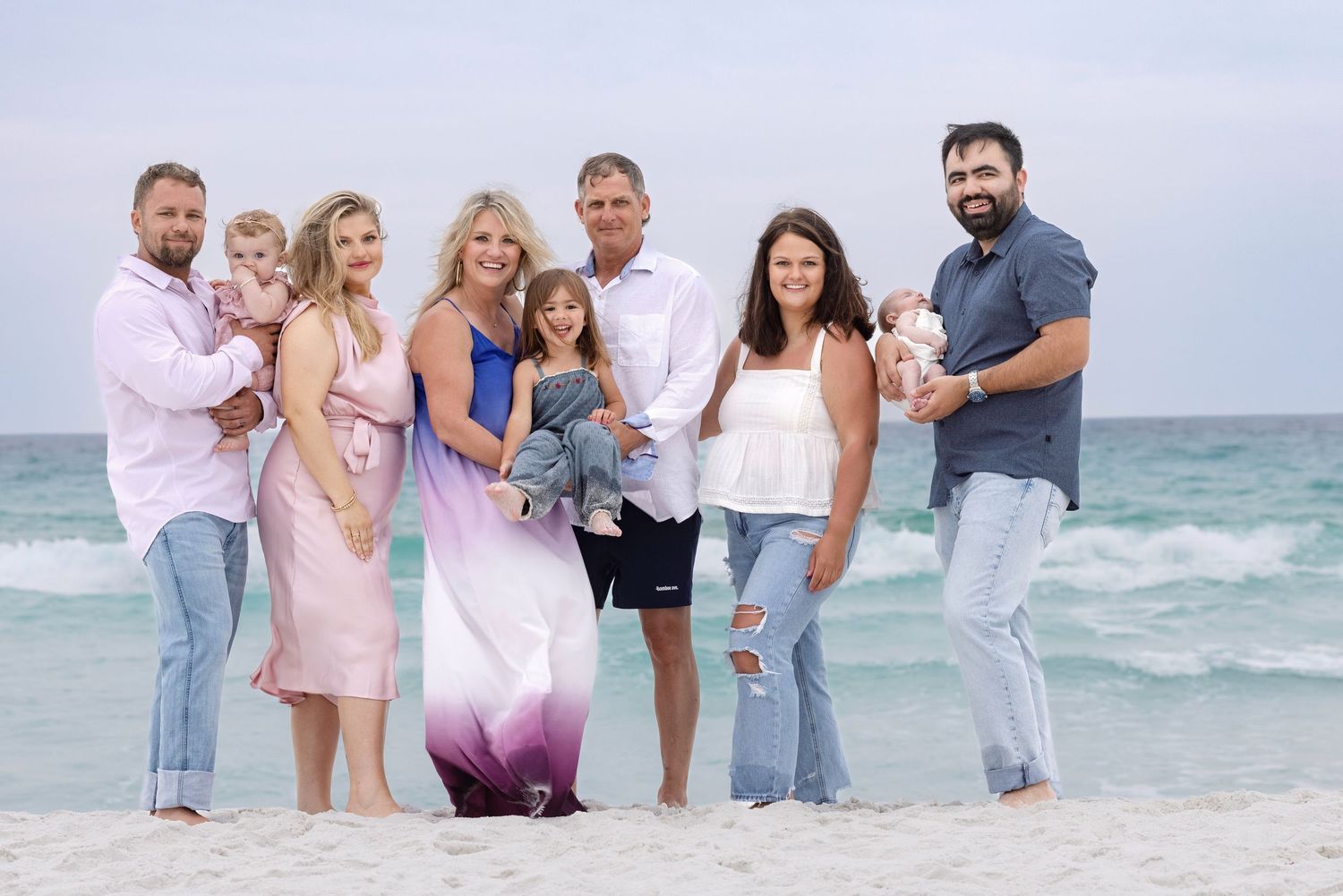 Large family group posing together on a white sand beach with turquoise ocean waves in the background.