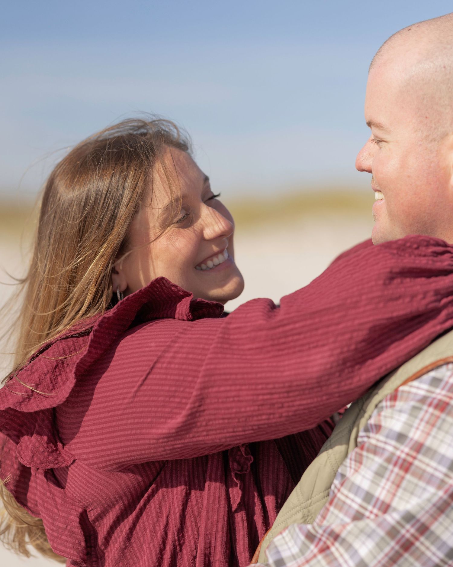 A couple in casual attire share a tender moment outdoors against a bright, natural background.
