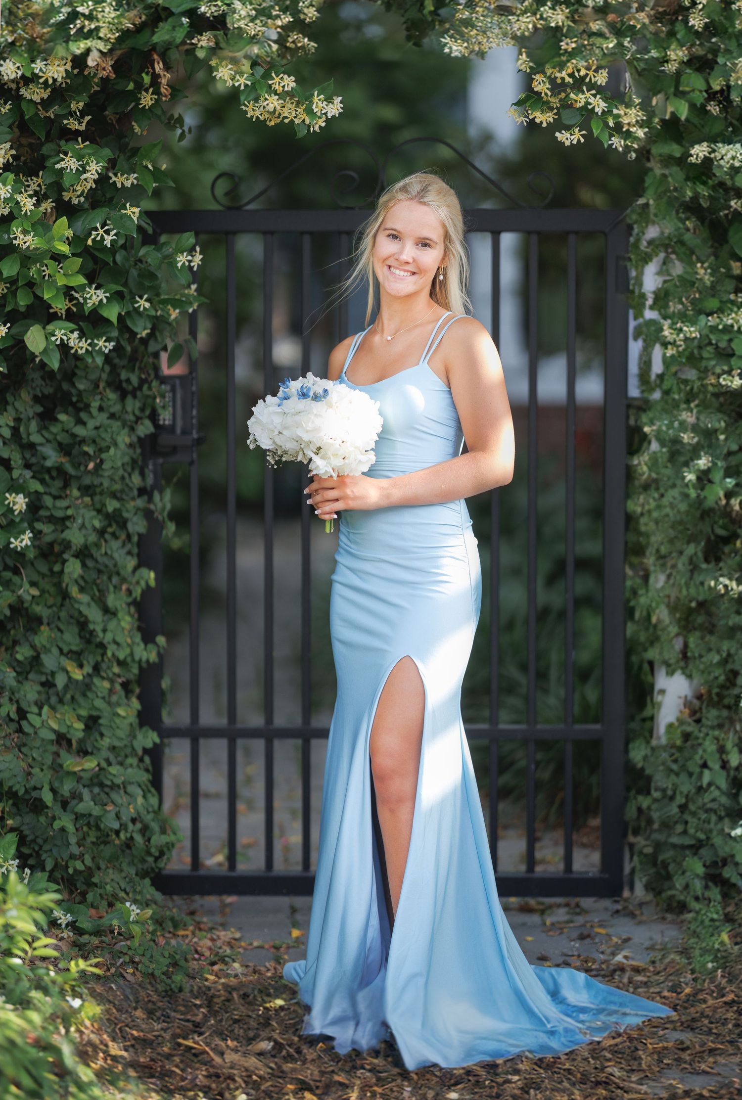 An elegant photo session featuring a light blue formal dress against an iron gate and greenery backdrop.
