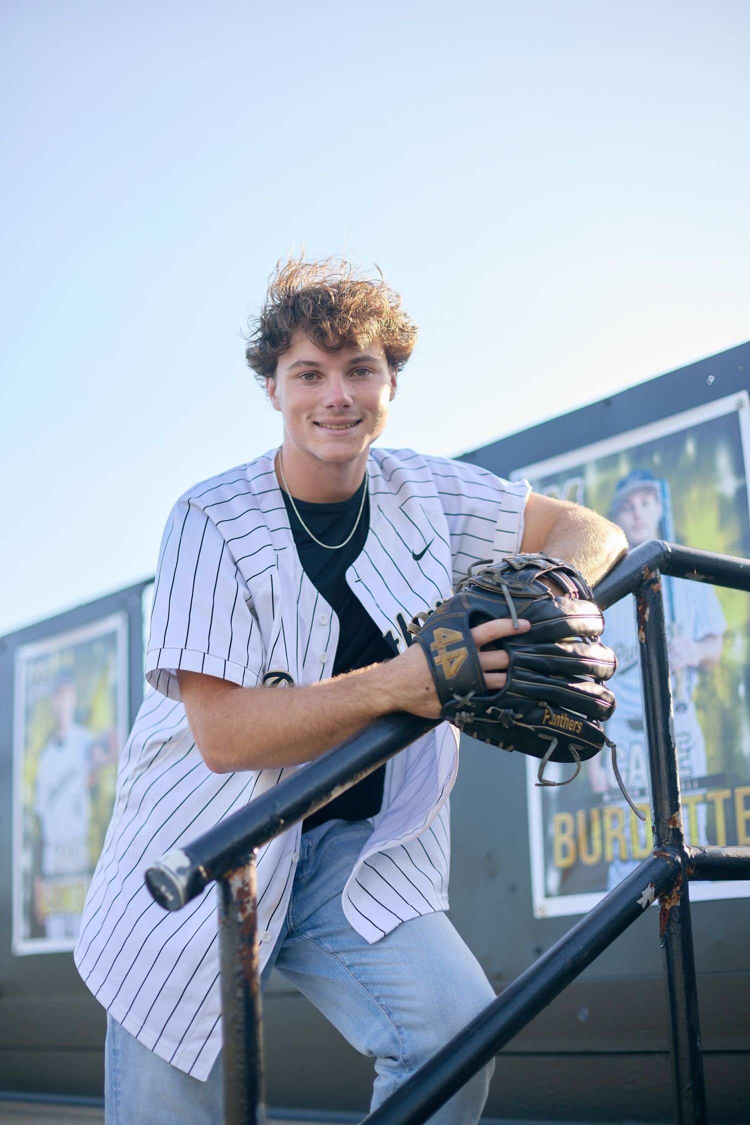 Baseball player in pinstriped uniform posing with glove against dugout railing on sunny day.