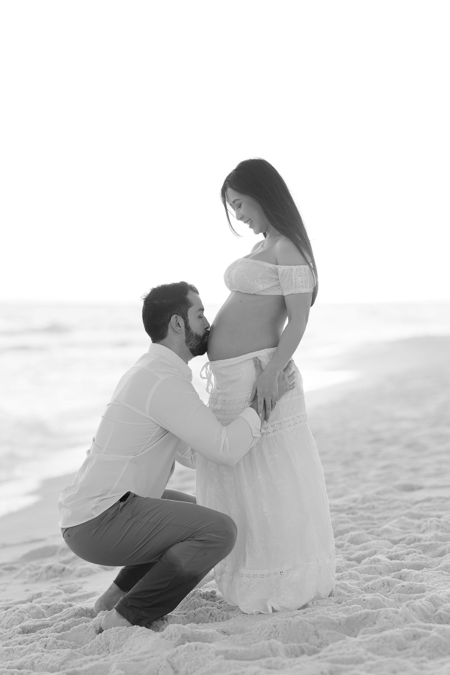 A couple sits together intimately on a sandy beach in a romantic black and white photo series.