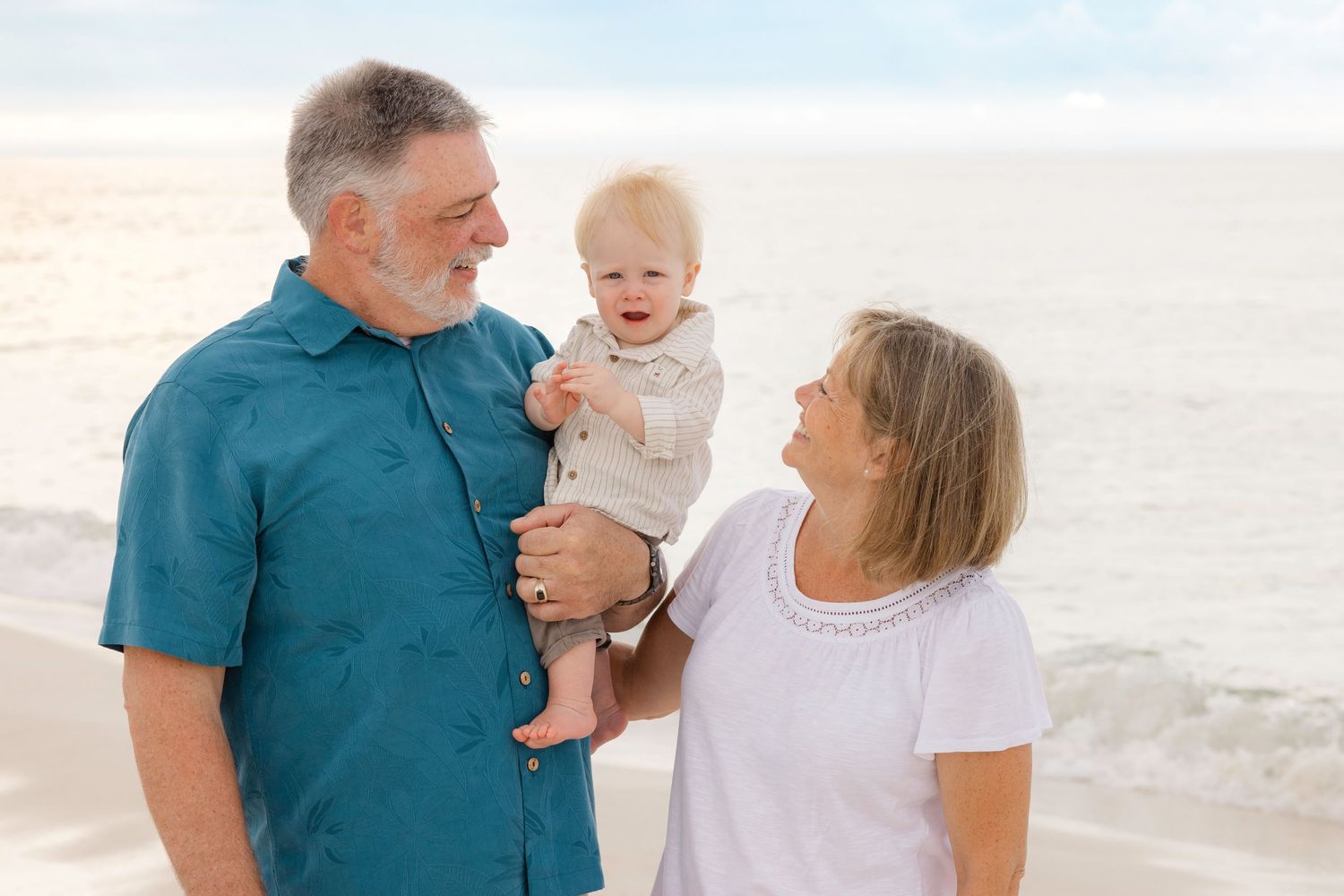 Family gathering on a white sandy beach at sunset with ocean waves in the background.