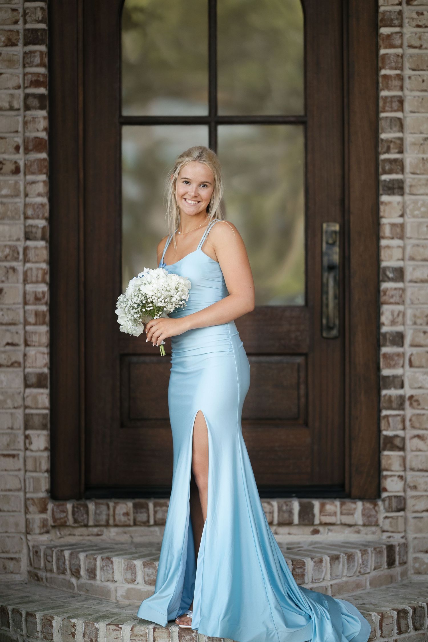 Elegant powder blue formal gown with slit and simple bouquet of baby's breath flowers on brick entryway steps.