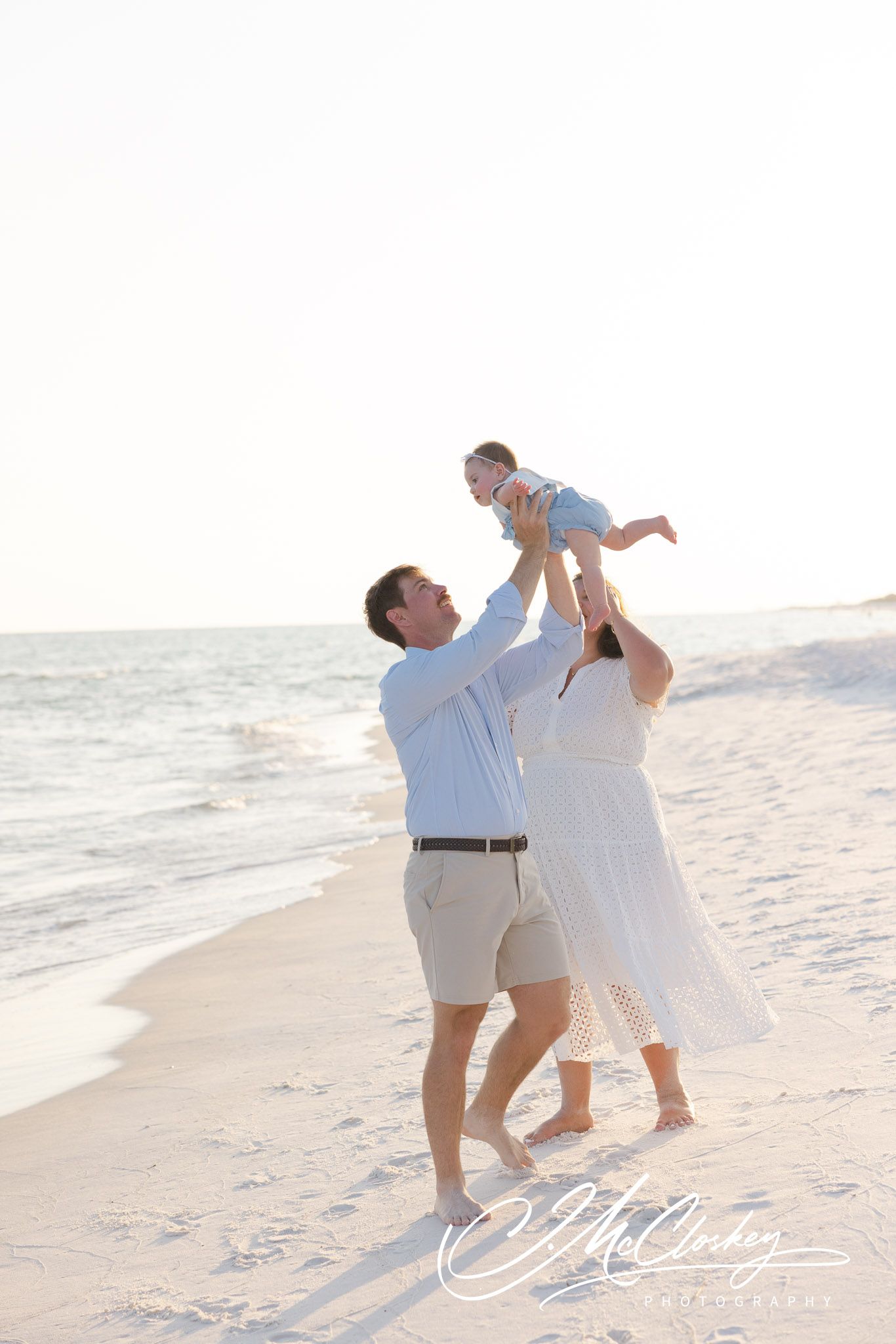 A family enjoys a tender moment playing together on a white sandy beach at sunset.