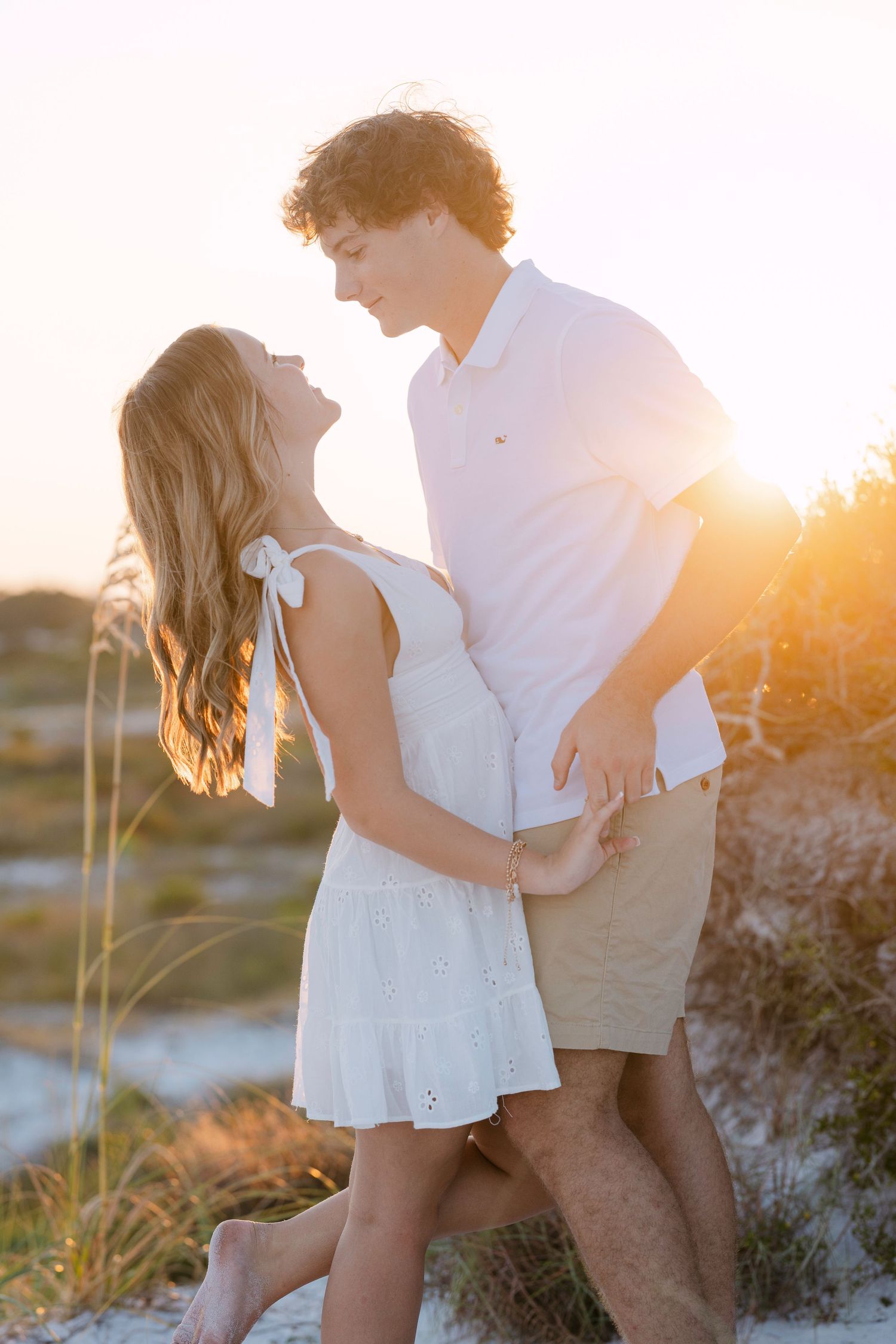 Romantic couple embraces on a beach at sunset with golden light filtering through the background.
