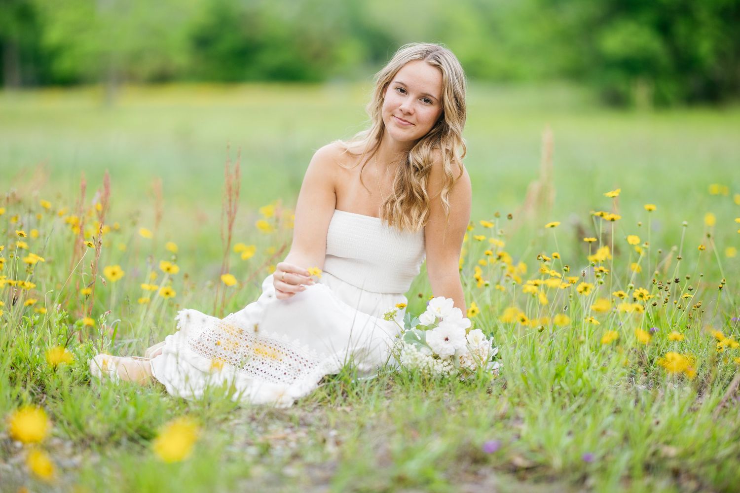 A person in a flowy white sundress reclines gracefully in a vibrant meadow filled with blooming yellow wildflowers.