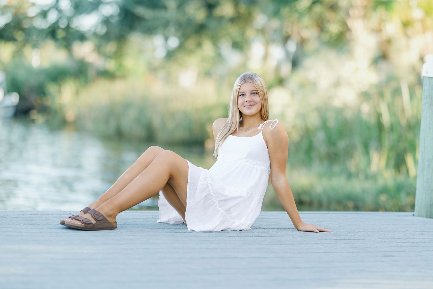 Four dreamy outdoor summer portraits featuring white sundress and casual poses by a serene waterfront setting.