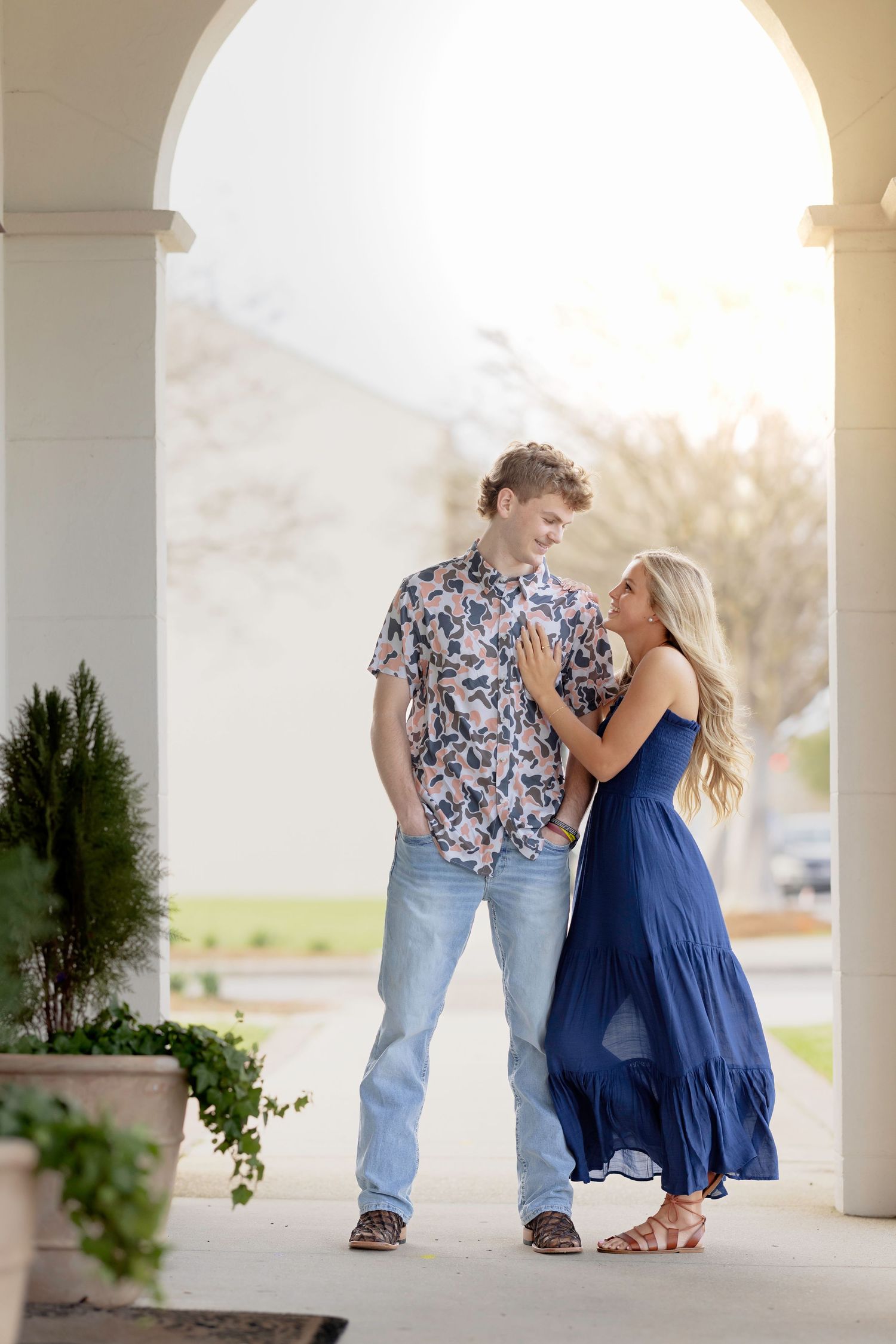 A parent and child in blue dress share tender moments under white pillared arches at sunset.