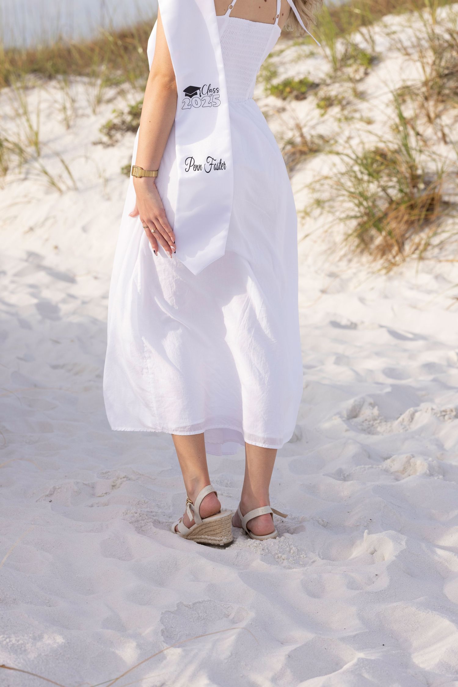 Close-up view of sandals and white dress hem against soft beach sand.