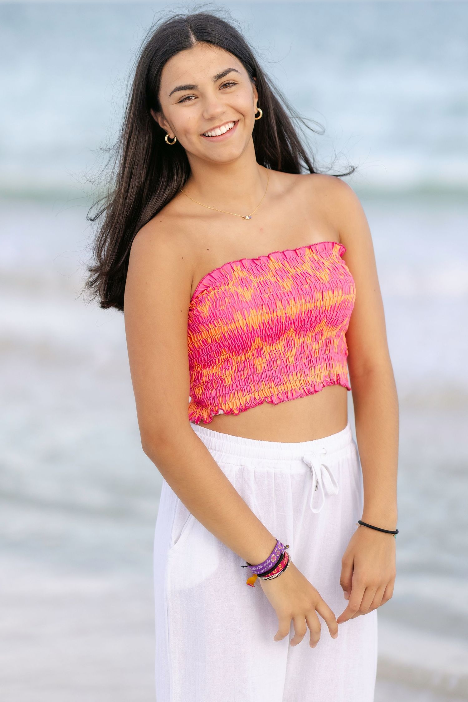 Beach portrait series featuring white pants and a pink patterned crop top against ocean waves.