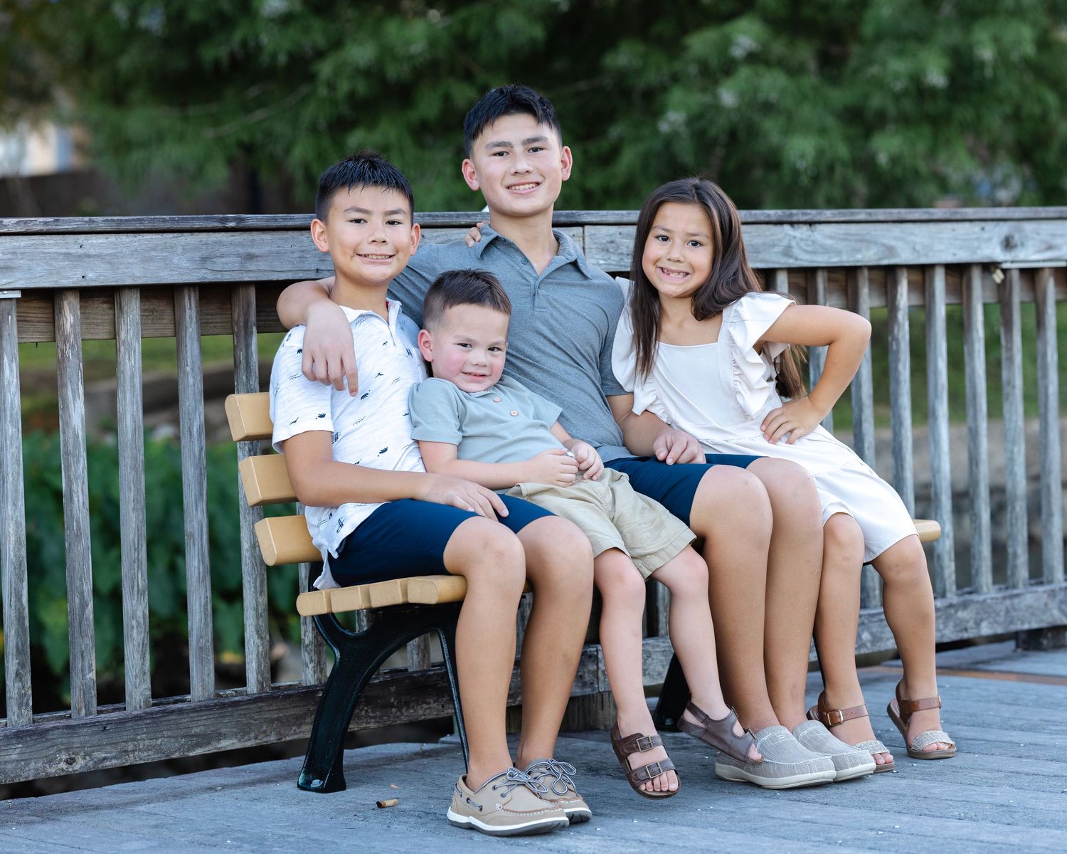 Family members sit together on a wooden pier bench, their legs dangling above the water on a sunny day.