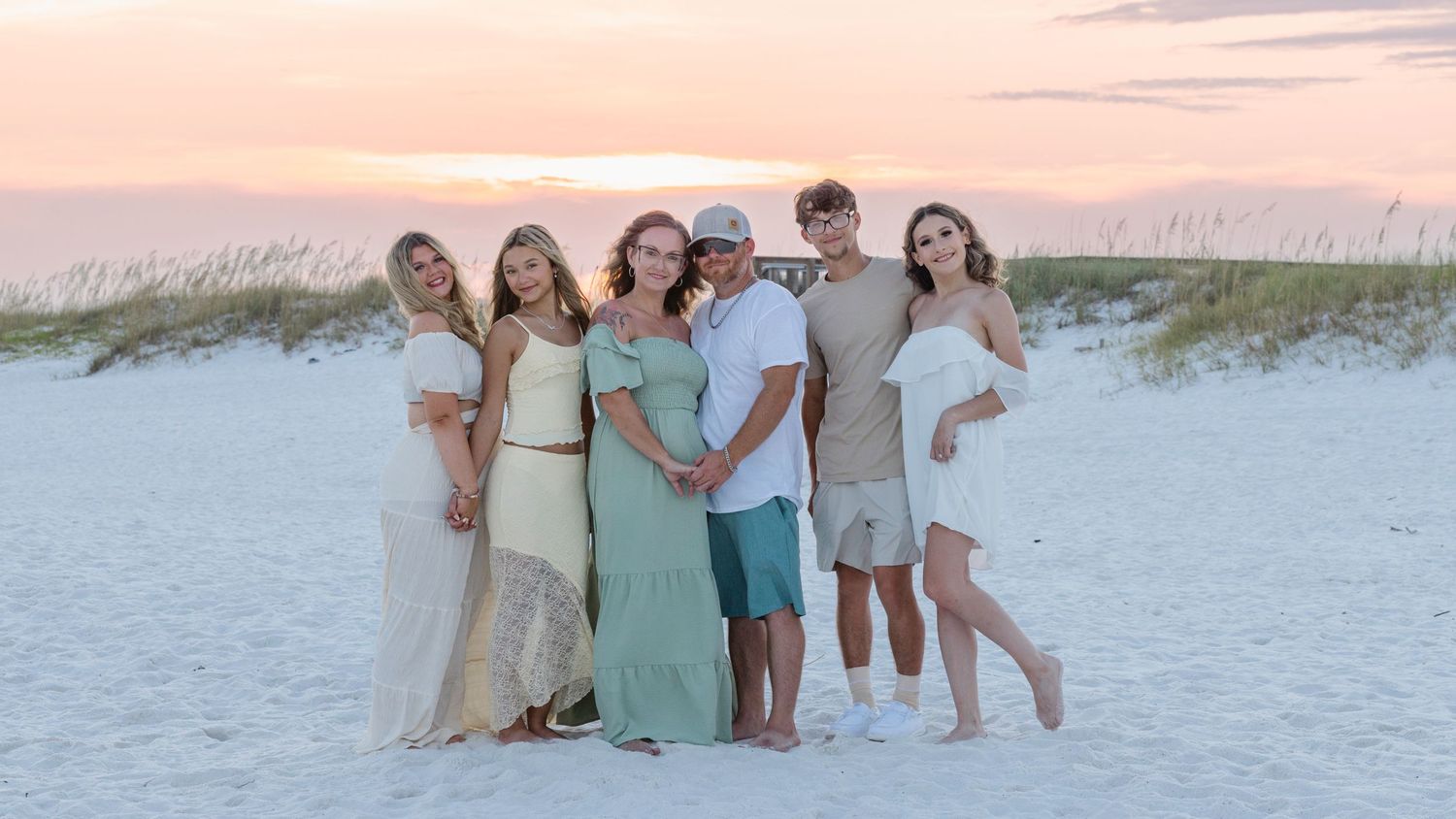 Group gathered on white sand beach at sunset wearing coordinated neutral-toned outfits.