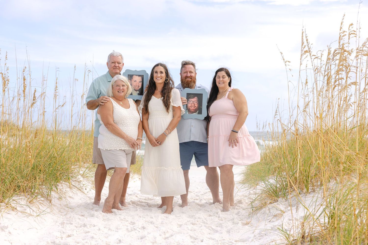 Multi-generational family group wearing coordinated beach outfits sits together on pristine white sand.