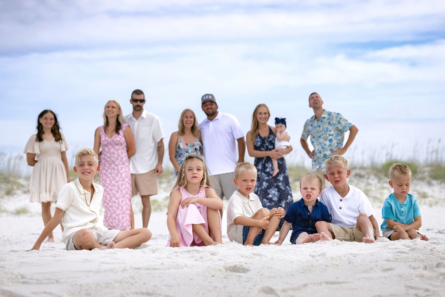 Large extended family group portrait on white sand beach, adults and children posing together outdoors.