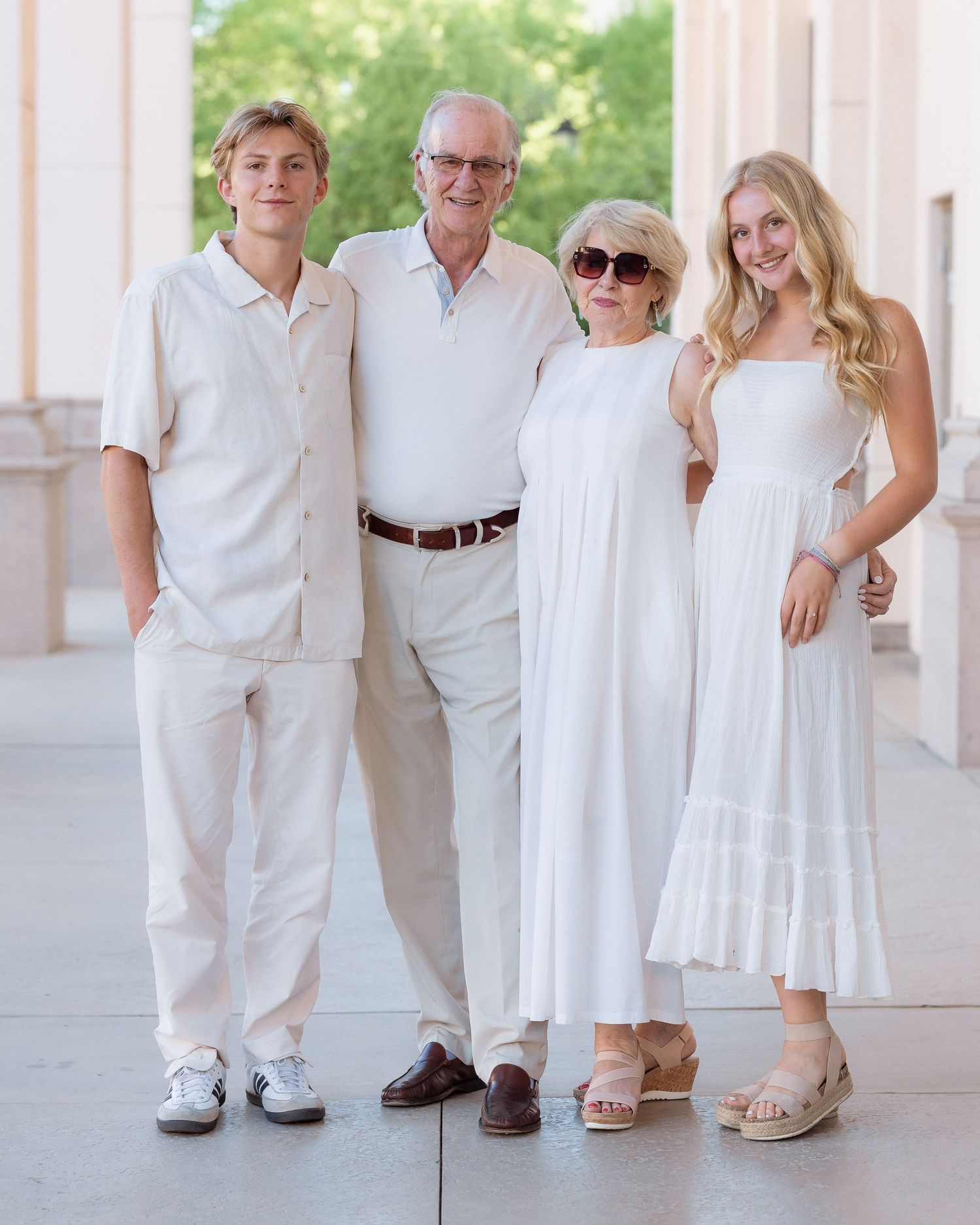 Four family members pose together in coordinated white outfits outdoors near elegant columns.