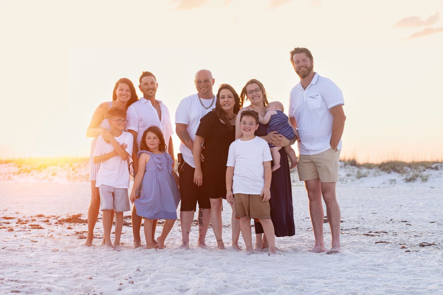 Large family posing together on a sandy beach at golden sunset, smiling for a portrait photo.