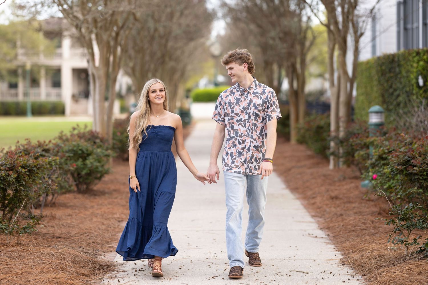 A couple walking hand in hand down a tree-lined pathway while wearing coordinated blue and floral outfits.