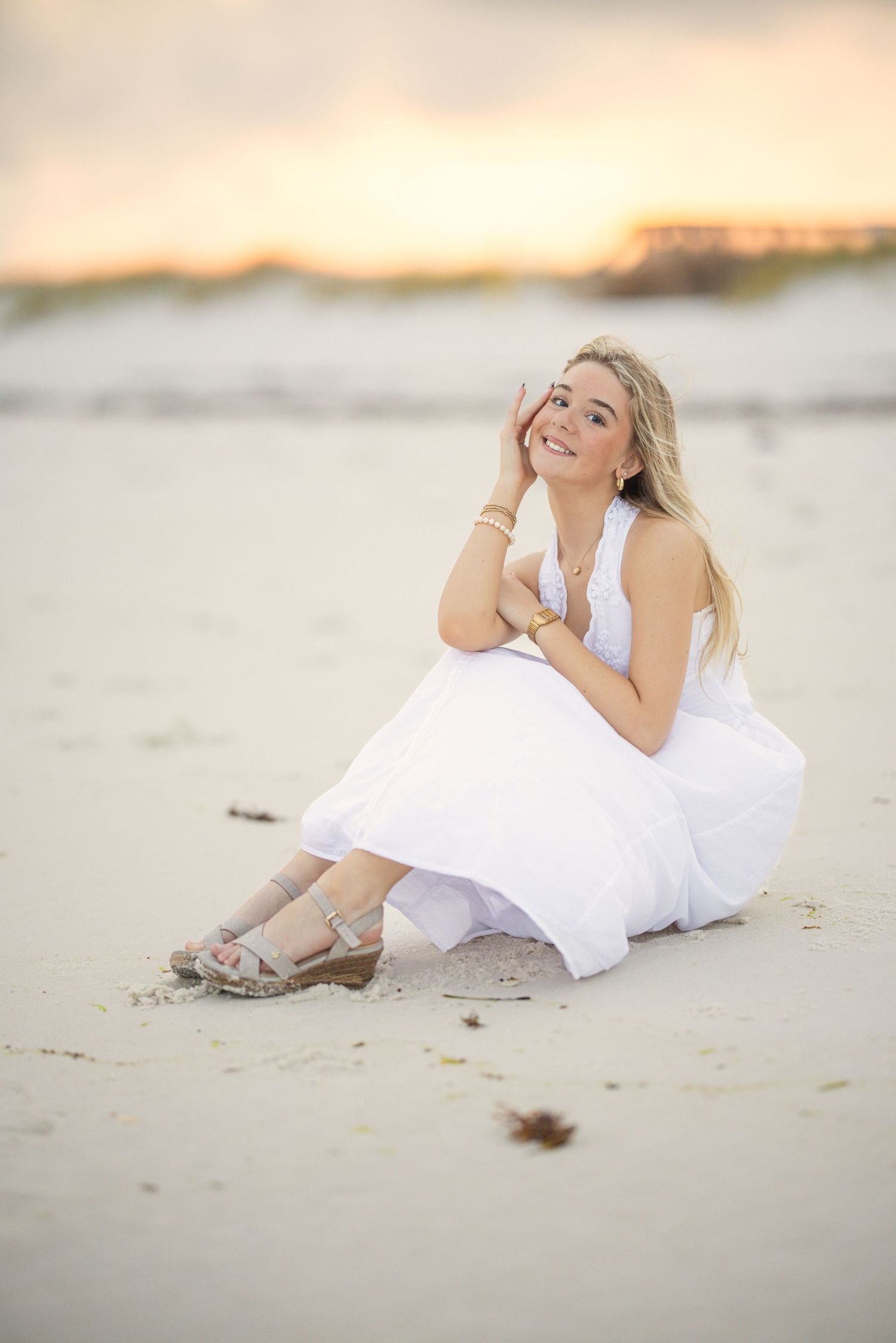 Figure in white dress lounges on beach sand during golden hour sunset.