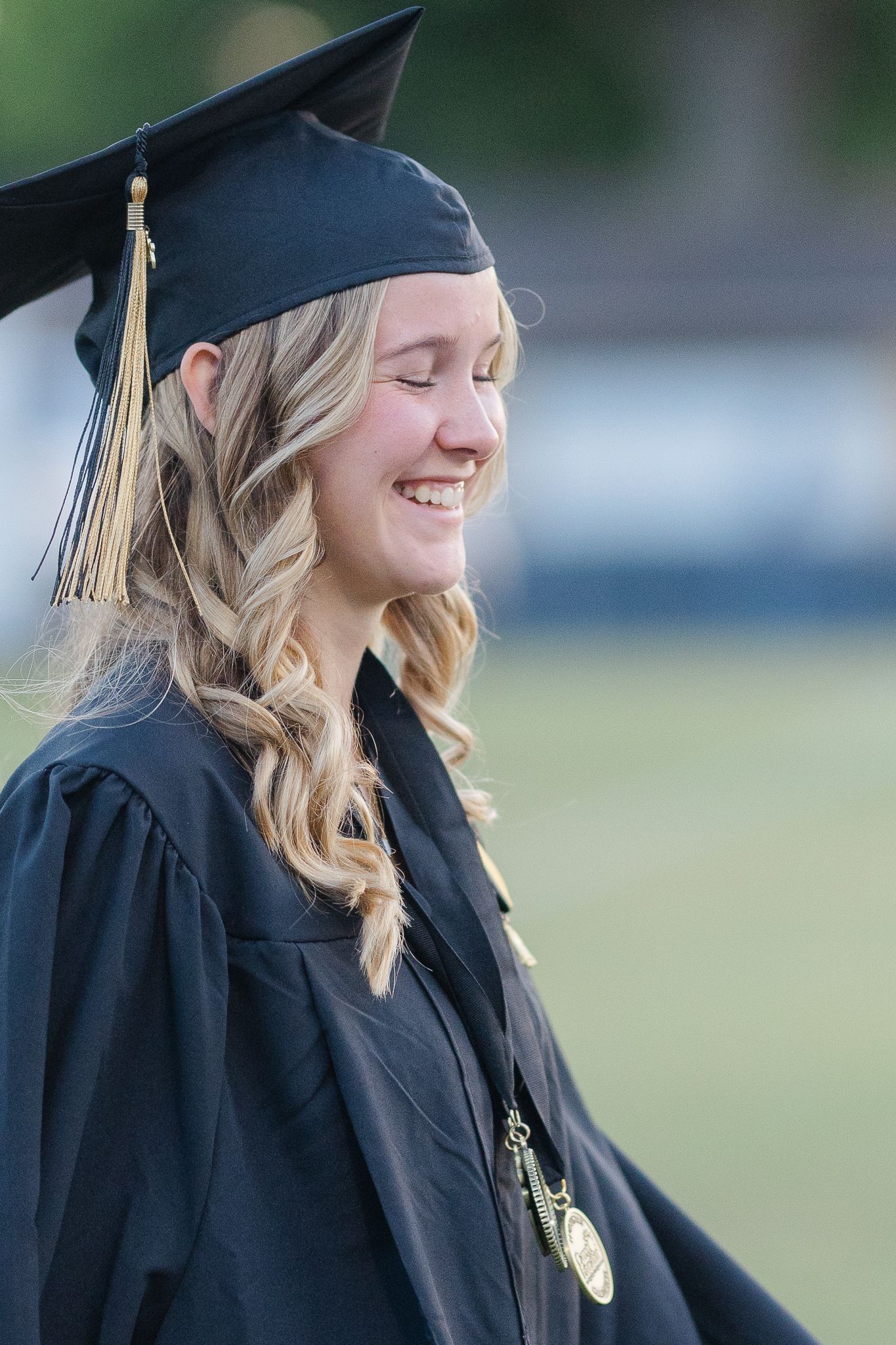 A graduate in academic dress smiles during an outdoor ceremony.