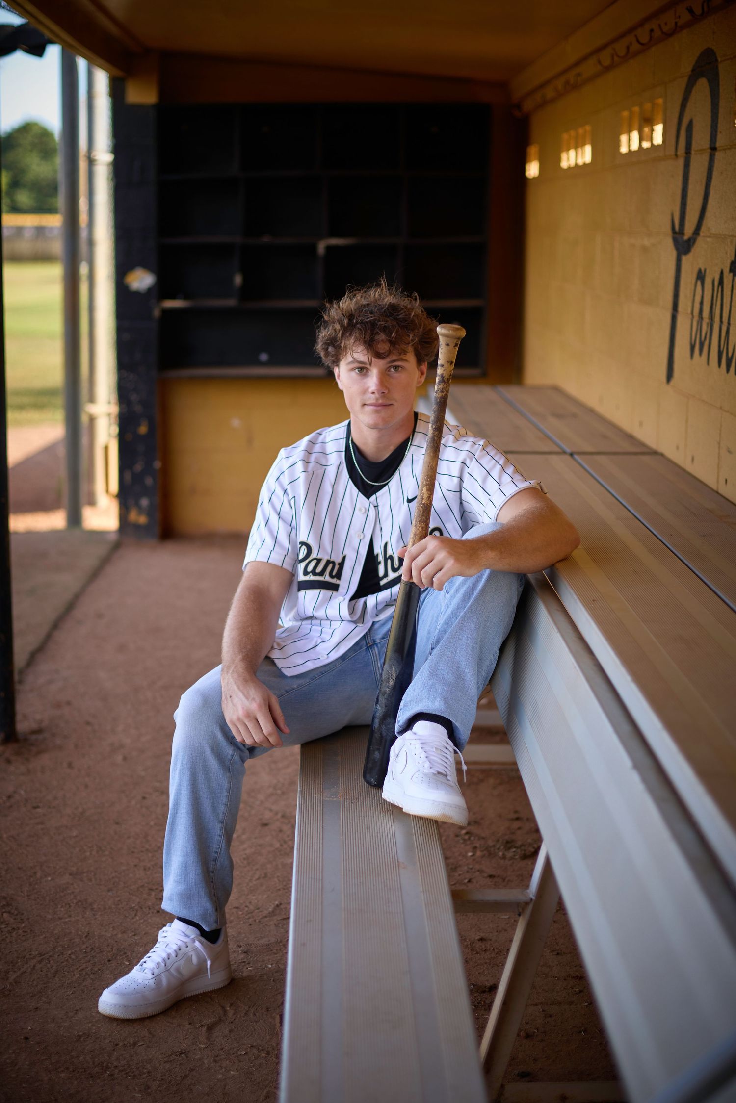 Baseball player sitting in dugout wearing pinstriped uniform and cleats.