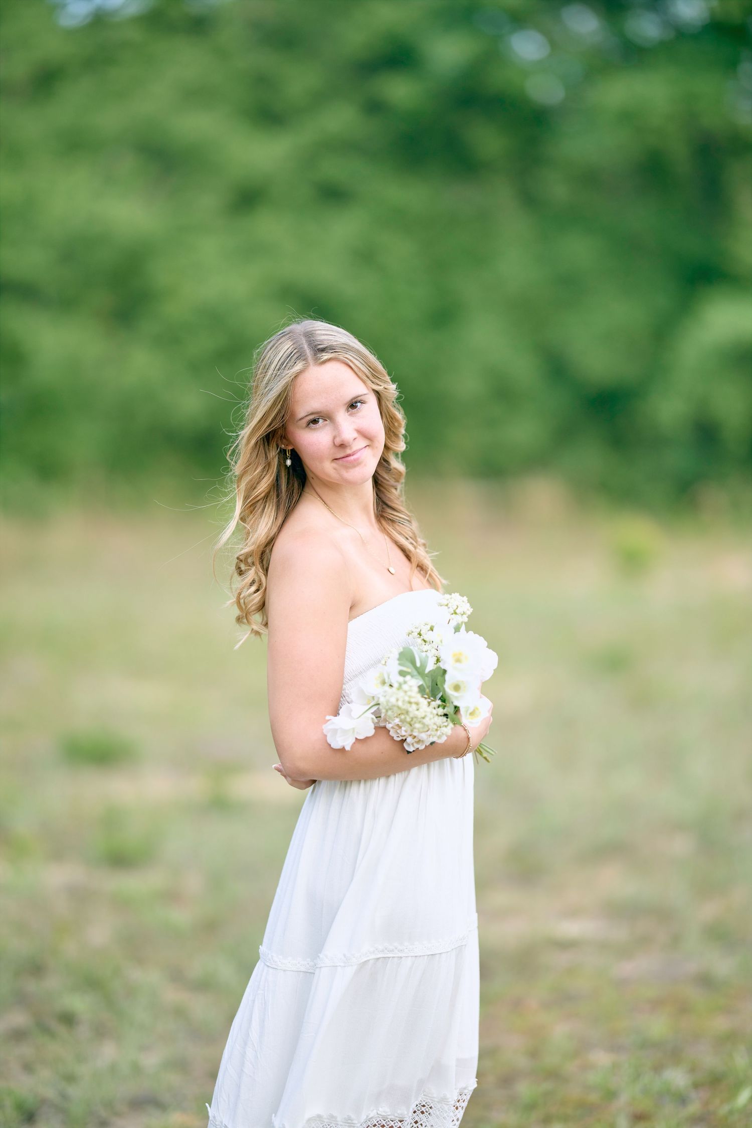Ethereal outdoor portrait with white dress and bouquet against green background.