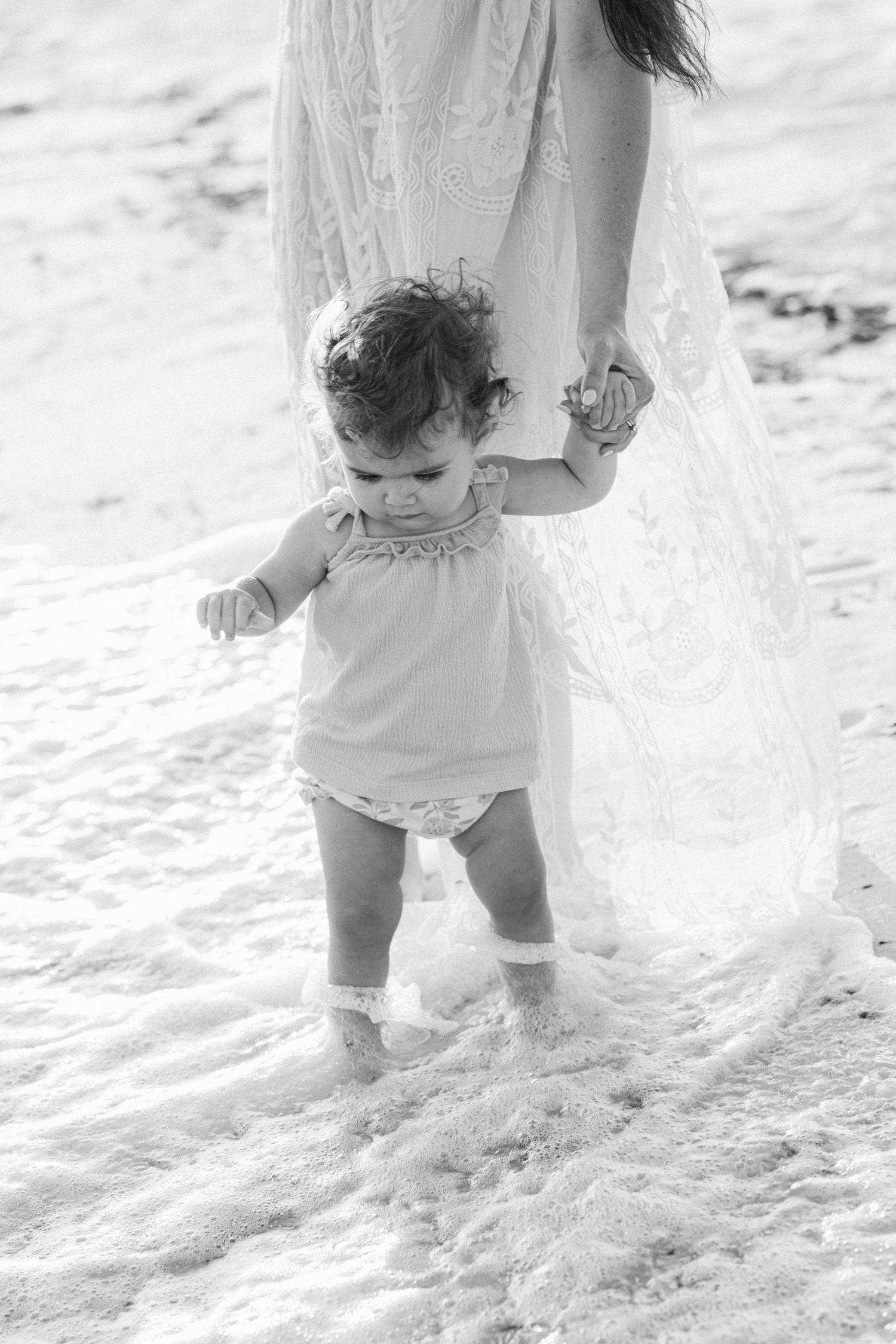 Black and white image of a small child's feet walking in the soft sand on a sunny beach.