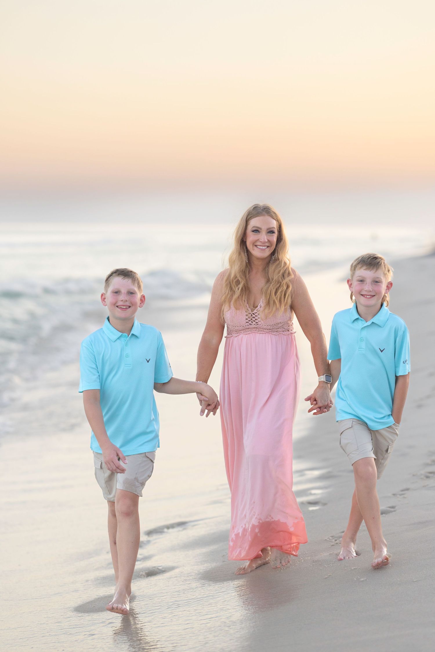 A family walking together along a sandy beach at sunset wearing matching blue and pink outfits.