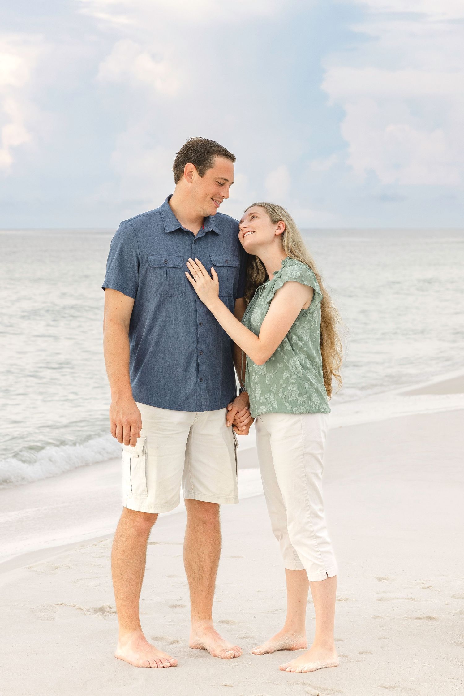 A couple embraces on a serene beach with white sand and soft waves in the background.