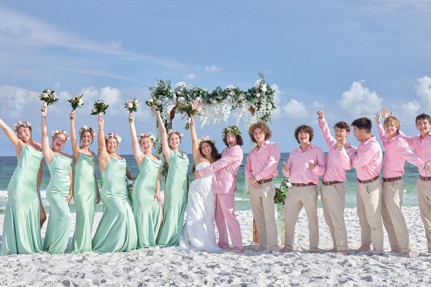 Beach wedding party in mint bridesmaid dresses and pink groomsmen shirts celebrating by the ocean.
