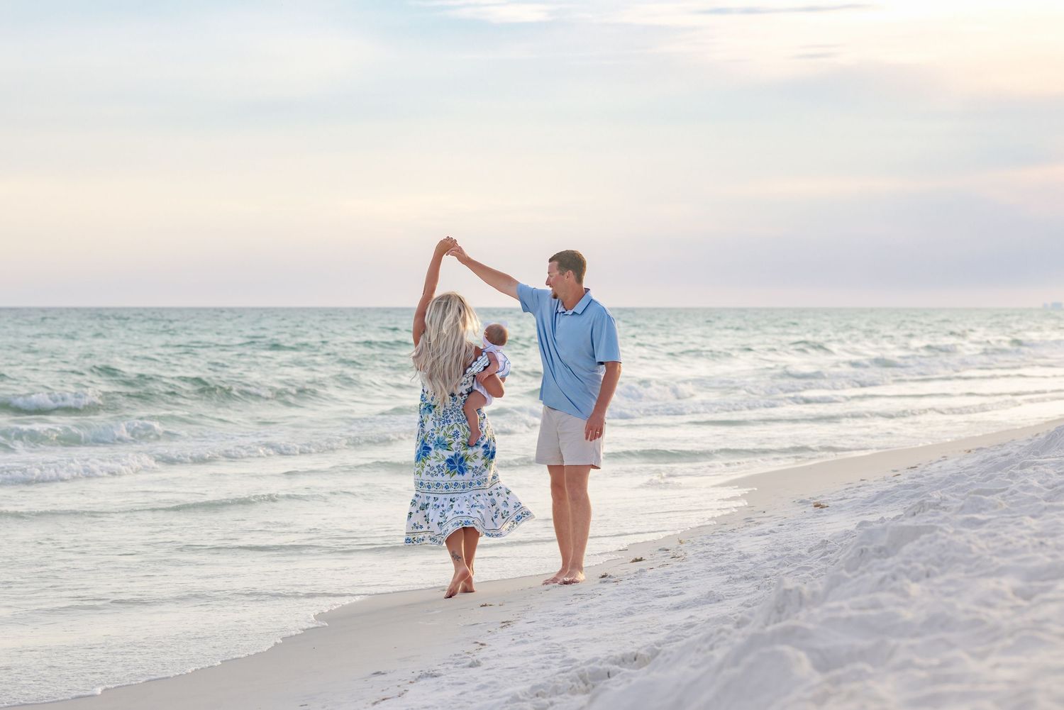 Couple dancing on a sandy beach at sunset with ocean waves in the background.