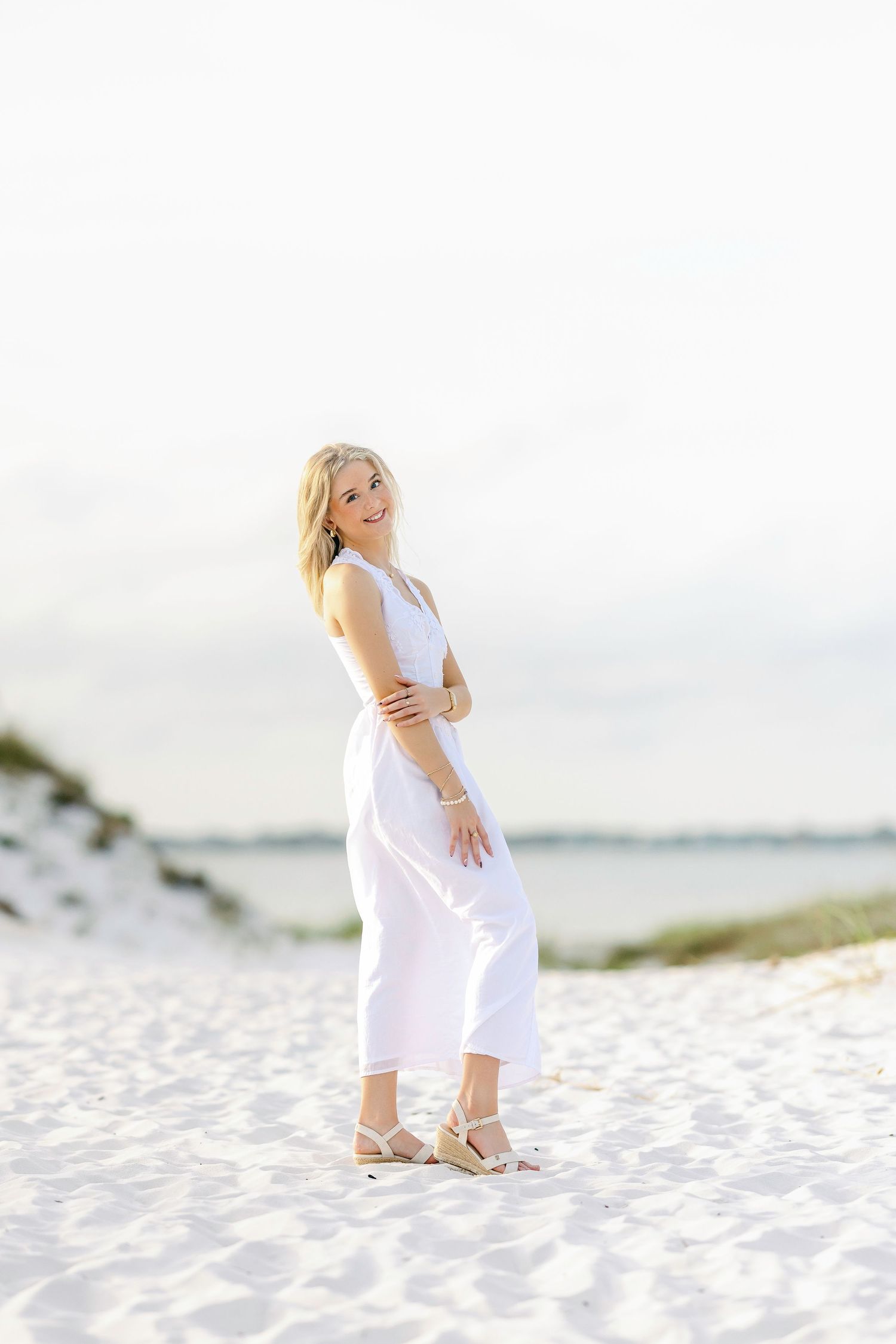 Bright coastal portrait featuring a white sleeveless dress against white sand dunes.