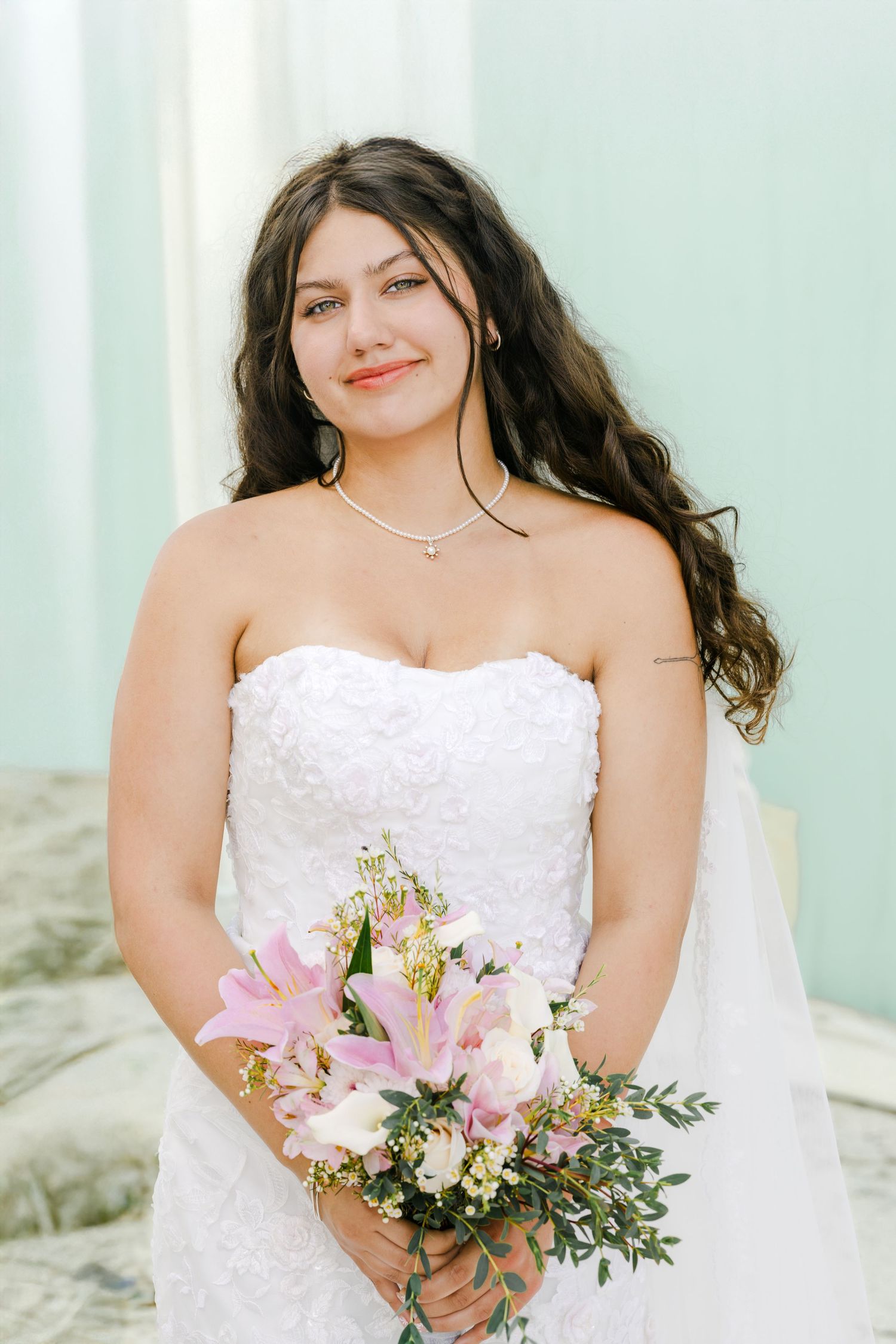 Person in white wedding dress holds pink lily bouquet.