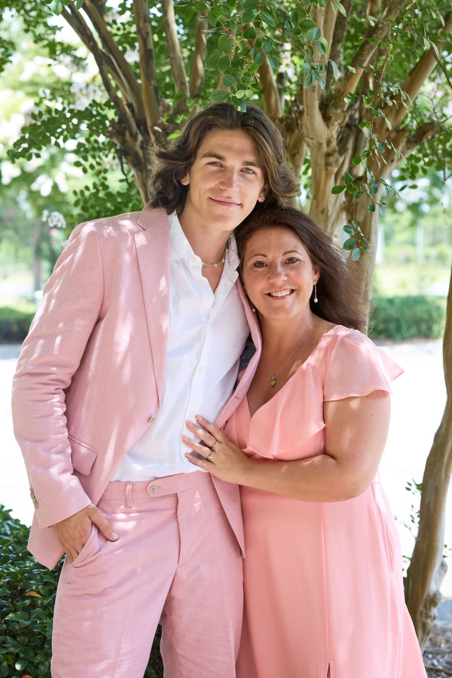 Couple in coordinating pink outfits pose together under dappled sunlight.