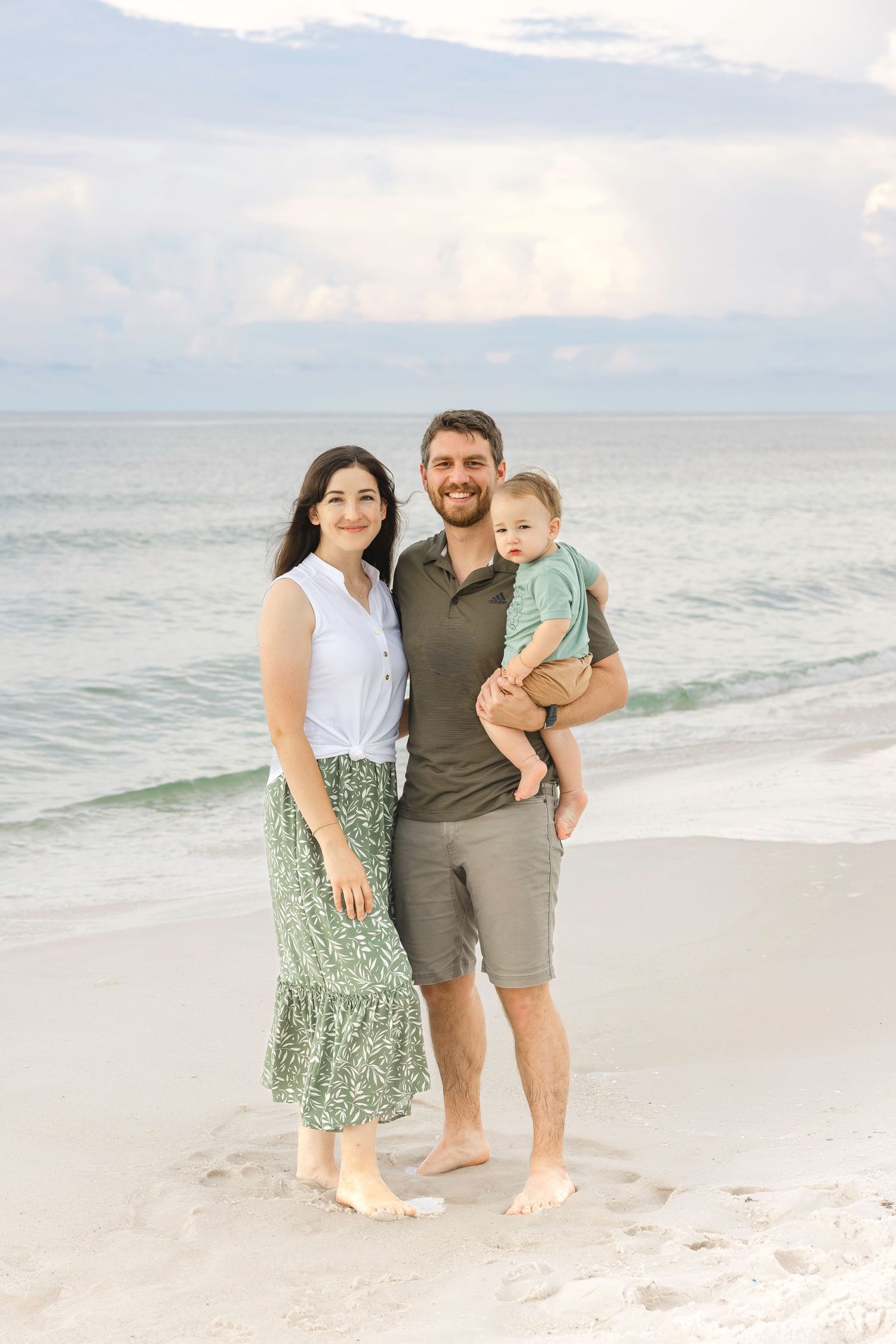 Family of three captures beach memories in casual attire with ocean waves and white sand backdrop.