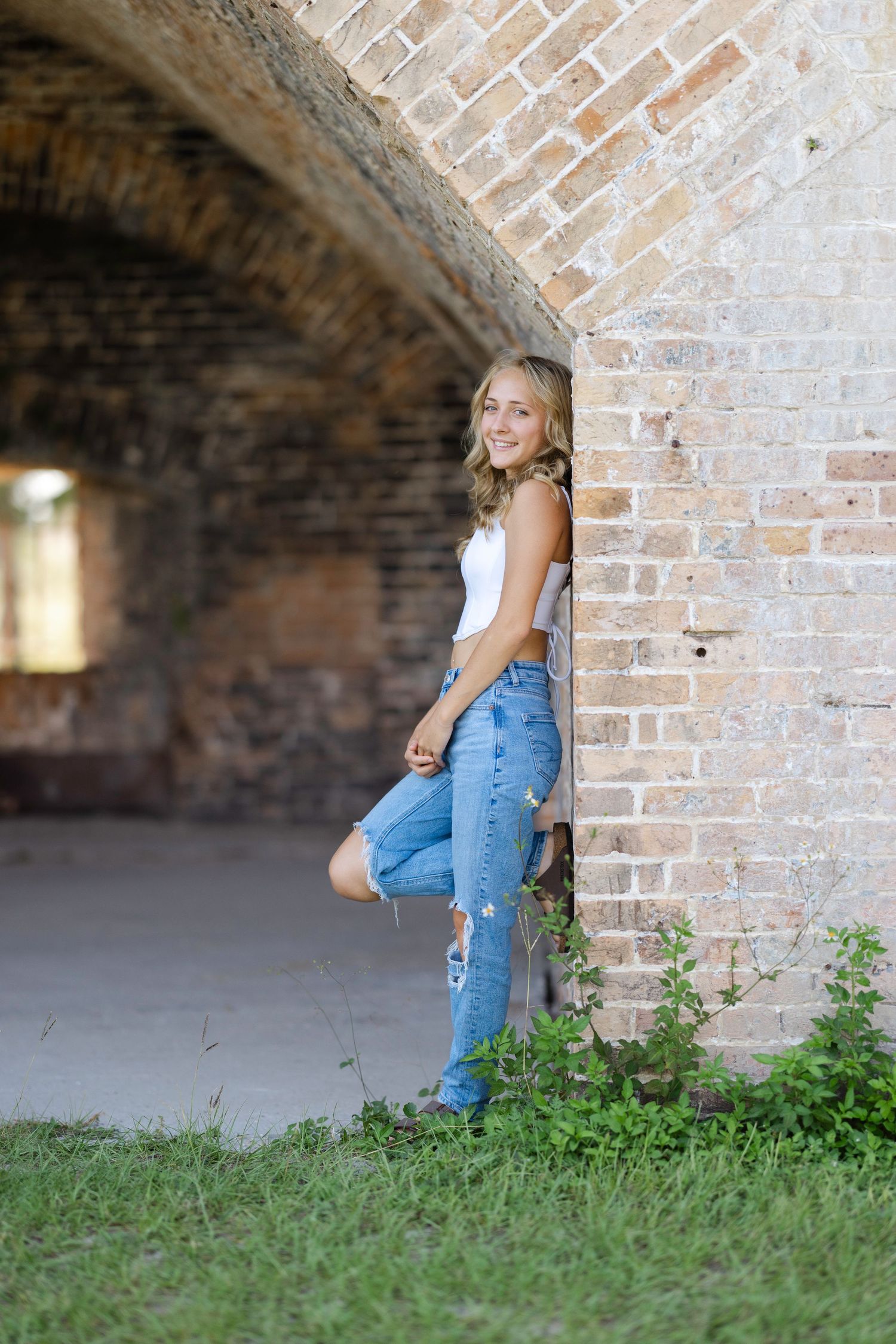 A casual portrait against a rustic brick archway features distressed jeans and a white top in an outdoor setting.