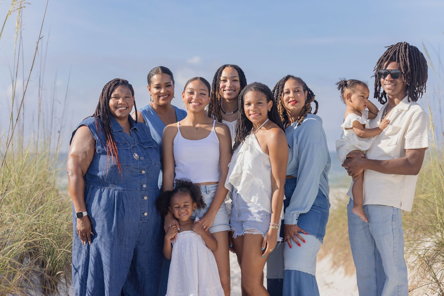 A joyful Black family group posing together on a sandy beach on a sunny day.