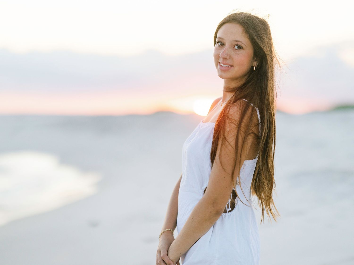 Woman in white dress stands on sandy beach during golden hour.